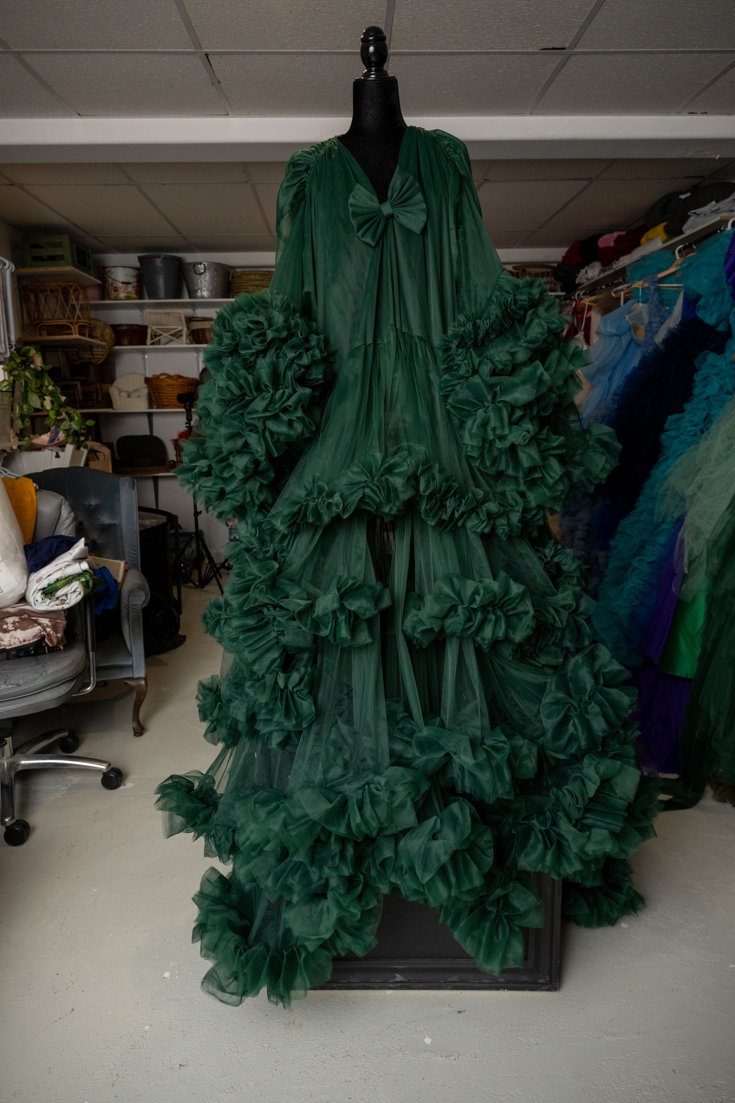 A dramatic emerald green tulle gown with voluminous ruffles displayed on a dress form in a studio setting.
