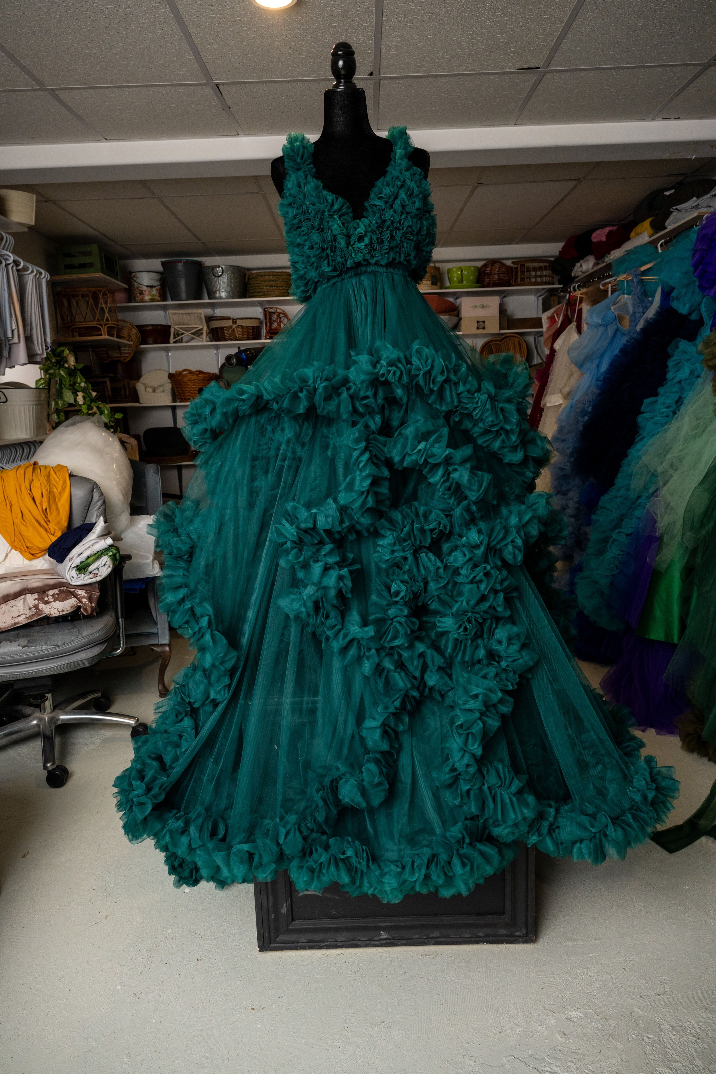 Emerald green ruffled tulle ball gown with layered skirt displayed on mannequin in storage room.