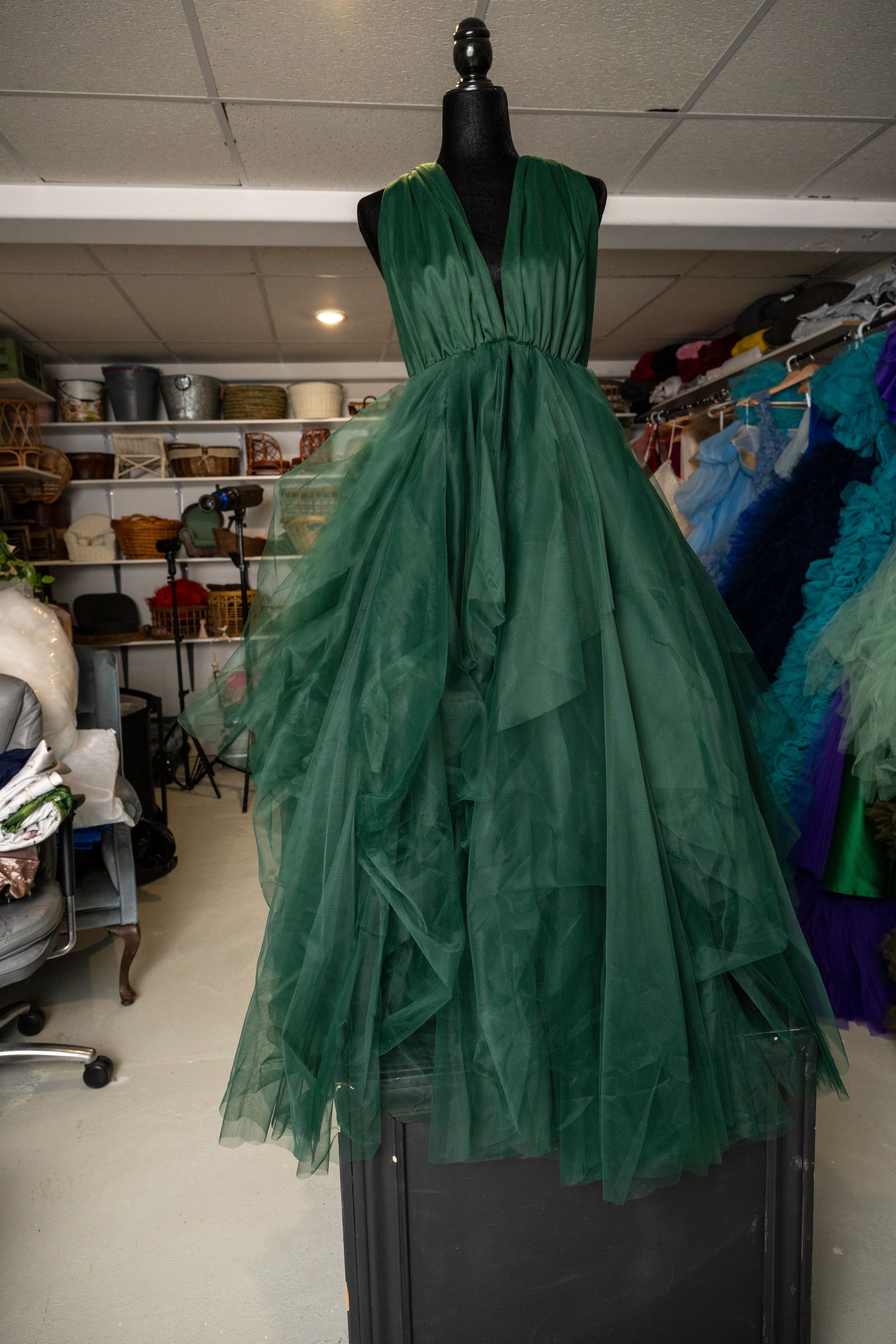 Flowing emerald green tulle dress with asymmetrical layers shown on dress form in storage space.