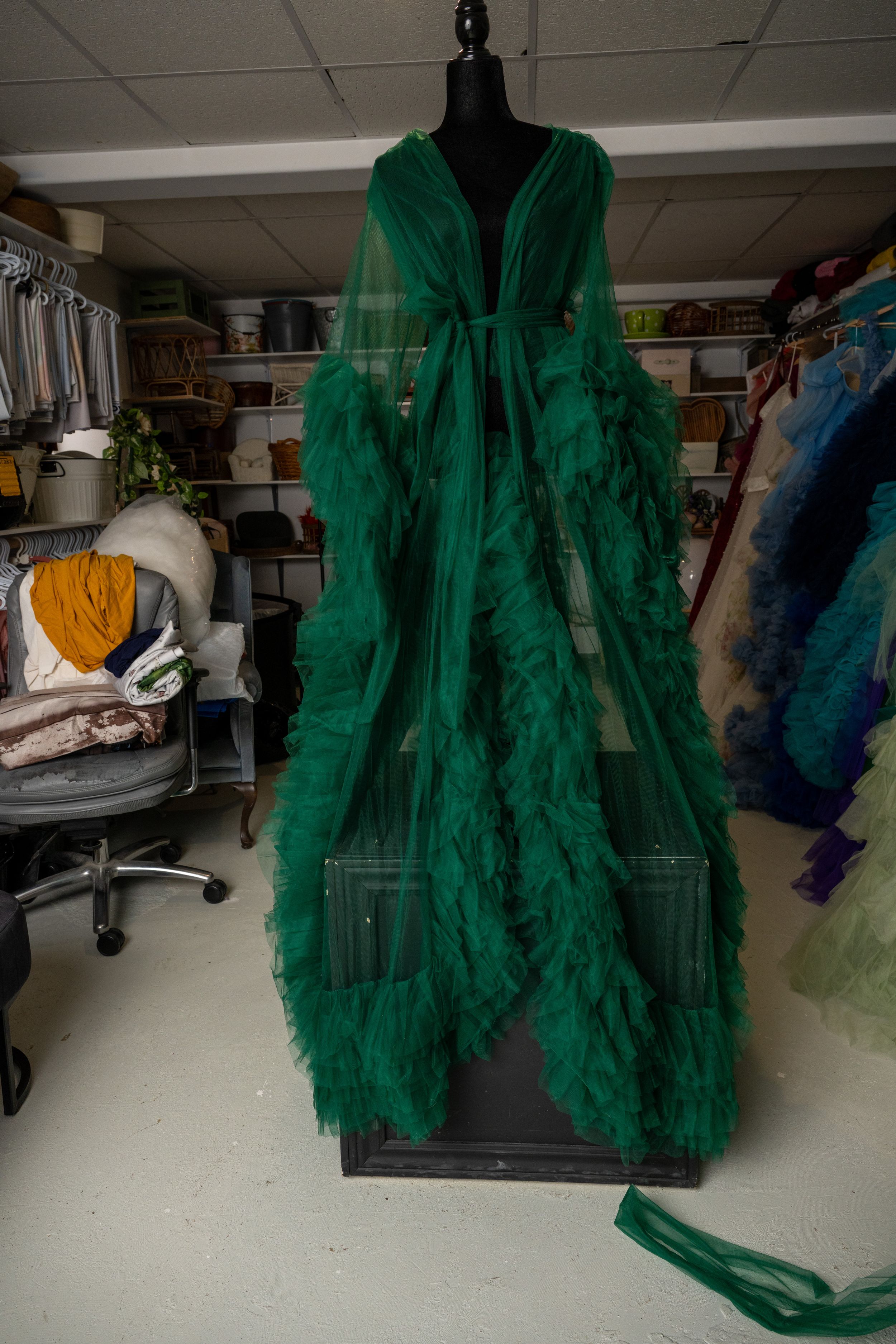 A bright emerald green tulle dress hangs on a black mannequin in what appears to be a costume storage area.