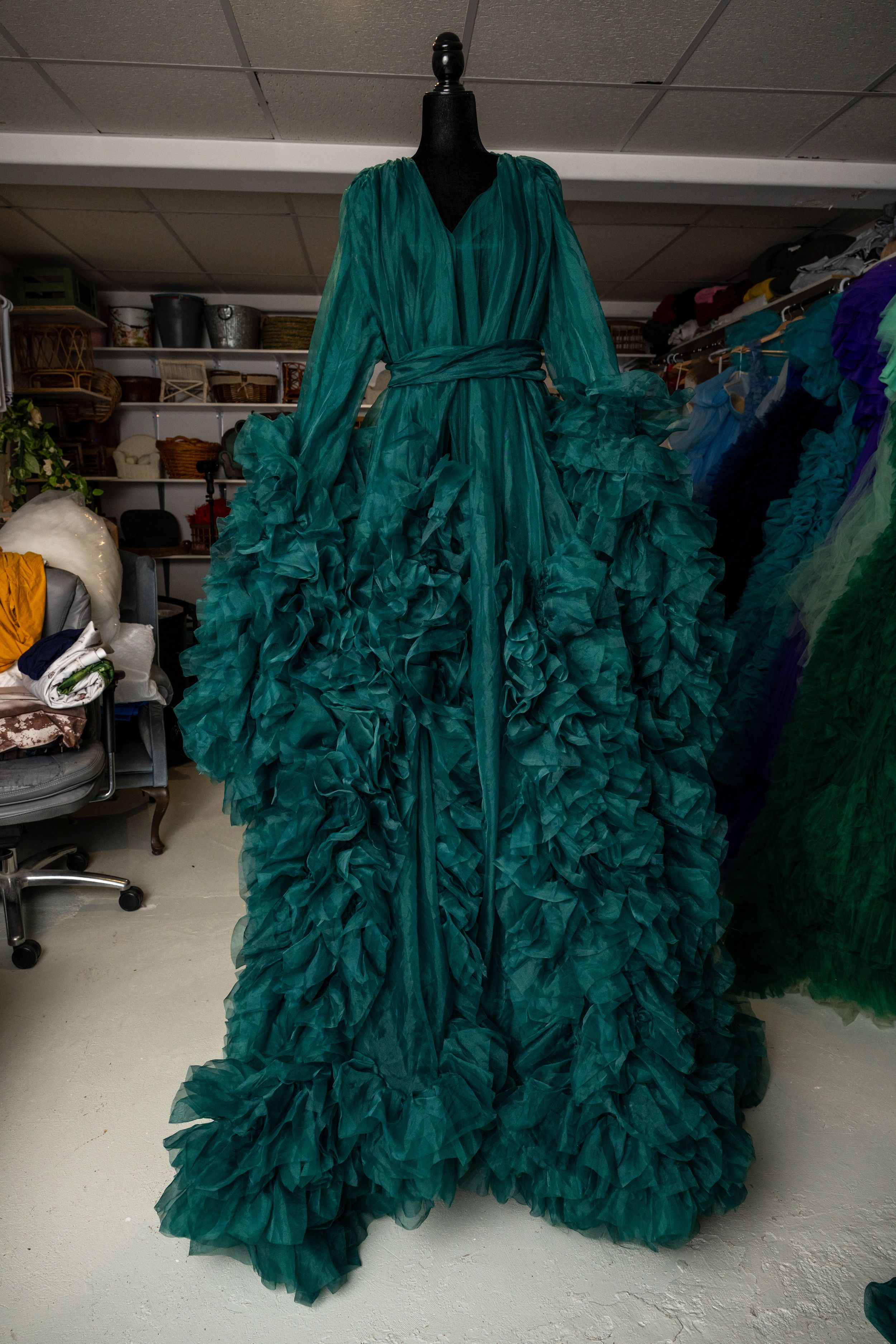 A dramatic emerald green ruffled ballgown with voluminous tiers shown from different angles in a clothing storage area.