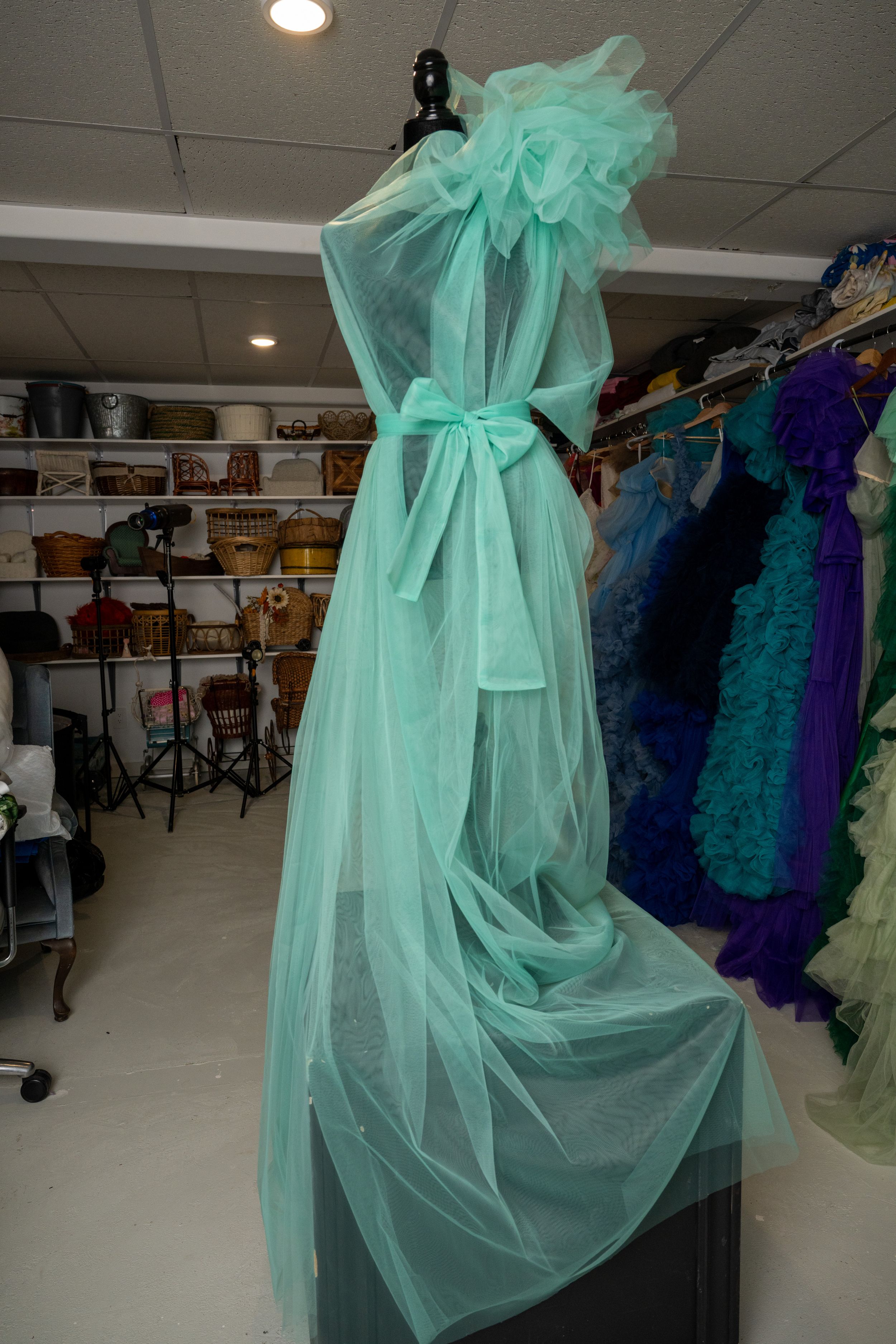 Elegant mint green formal dress with flowing tulle skirt and bow detail shown in a dress shop setting.
