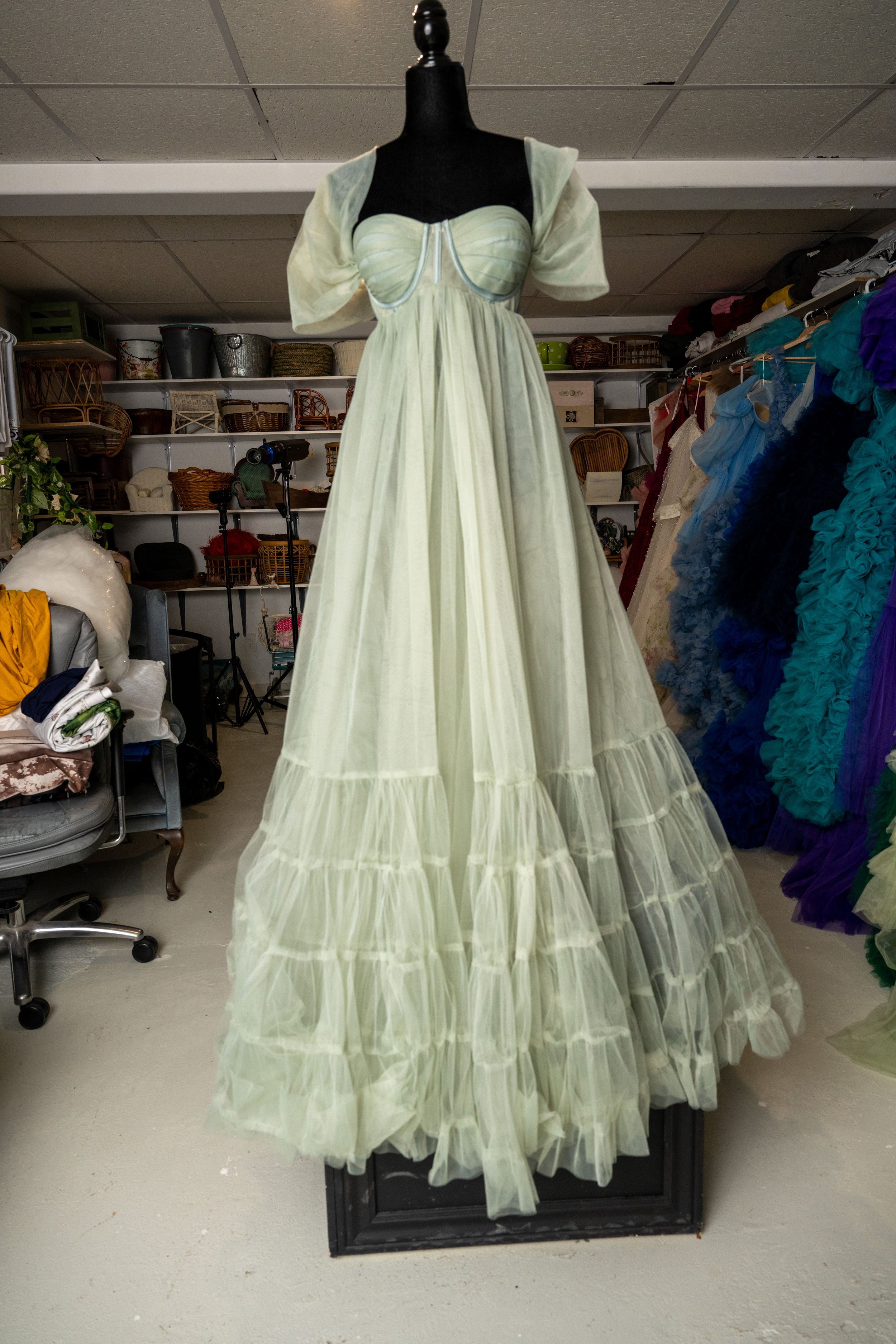 A light mint green petticoat with multiple ruffled layers displayed on a dress form in a storage space.