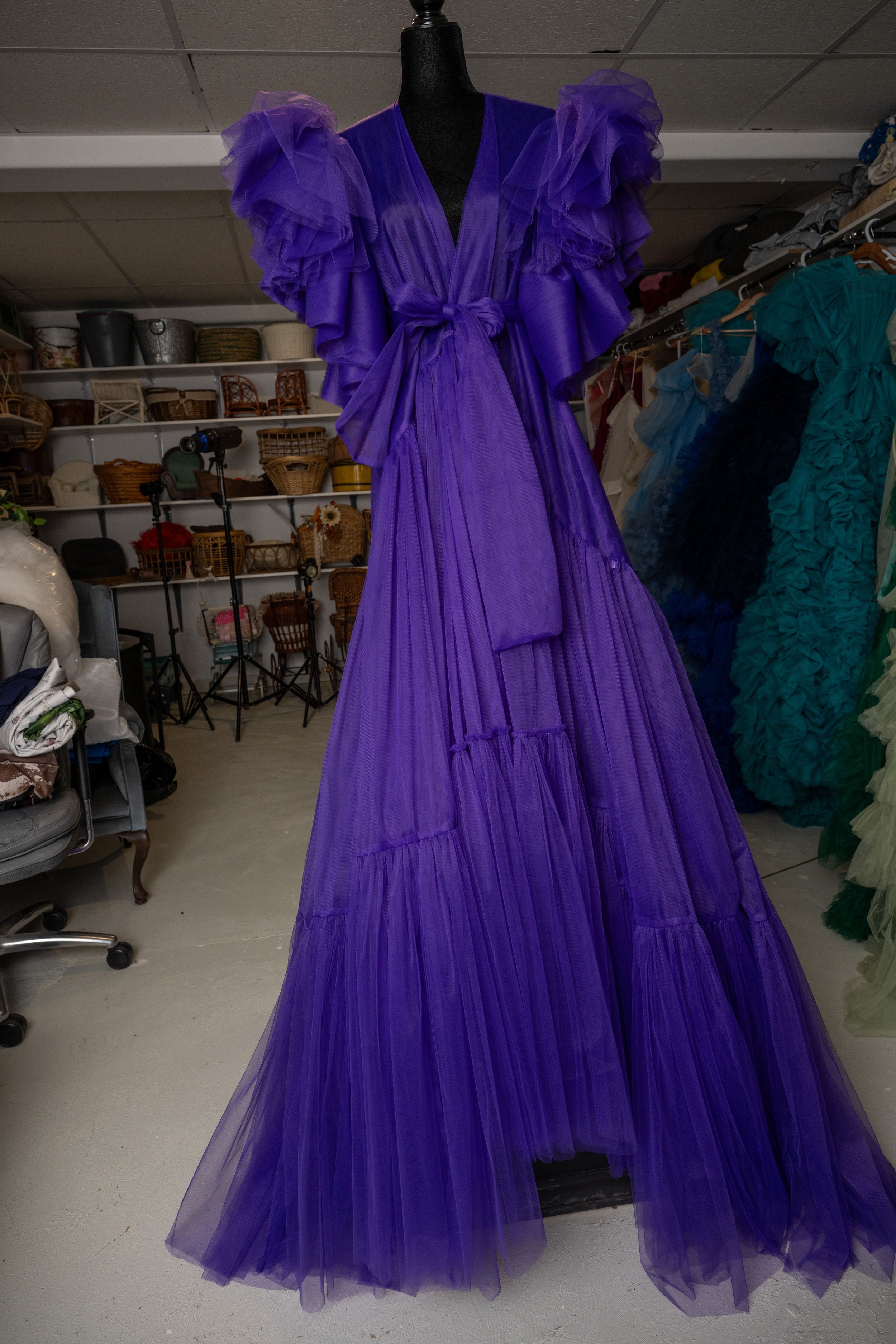 A vibrant purple tulle dress with ruffled layers and dramatic puff sleeves displayed on a black mannequin form.