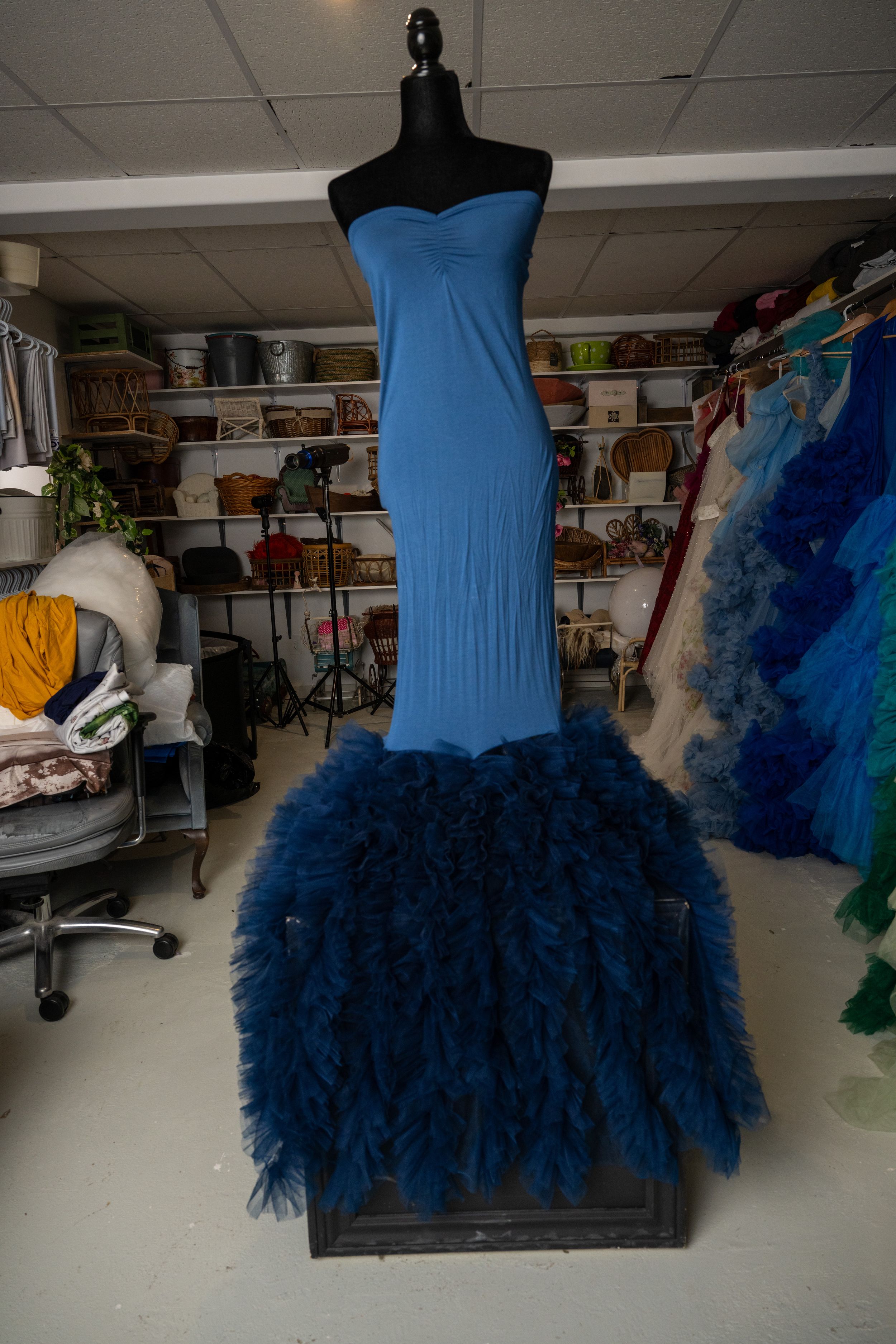 Navy blue formal dress with fitted bodice and voluminous tulle skirt displayed on mannequin in storage space.
