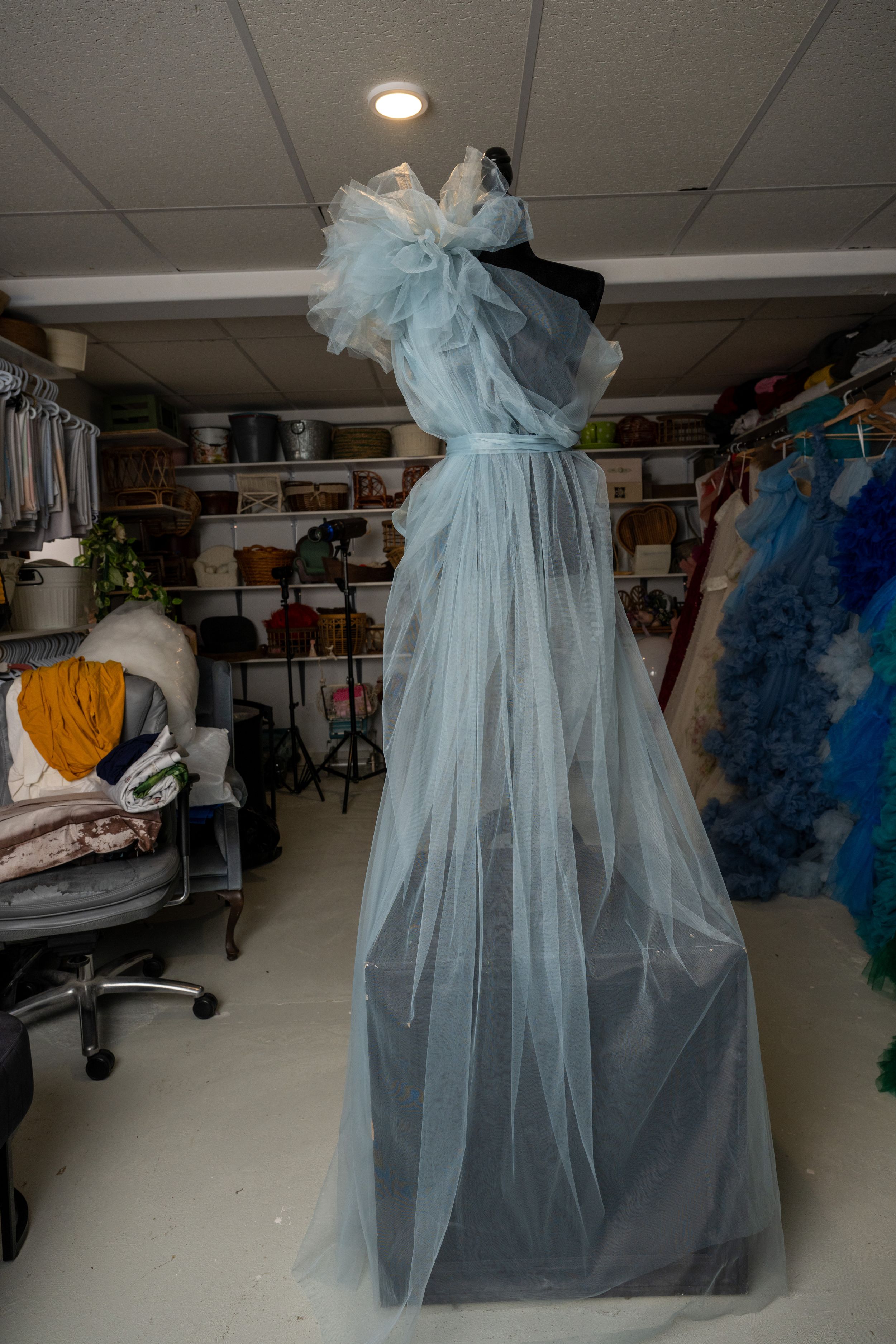 Light blue tulle dress with off-shoulder design displayed in a storage room setting with various items visible.