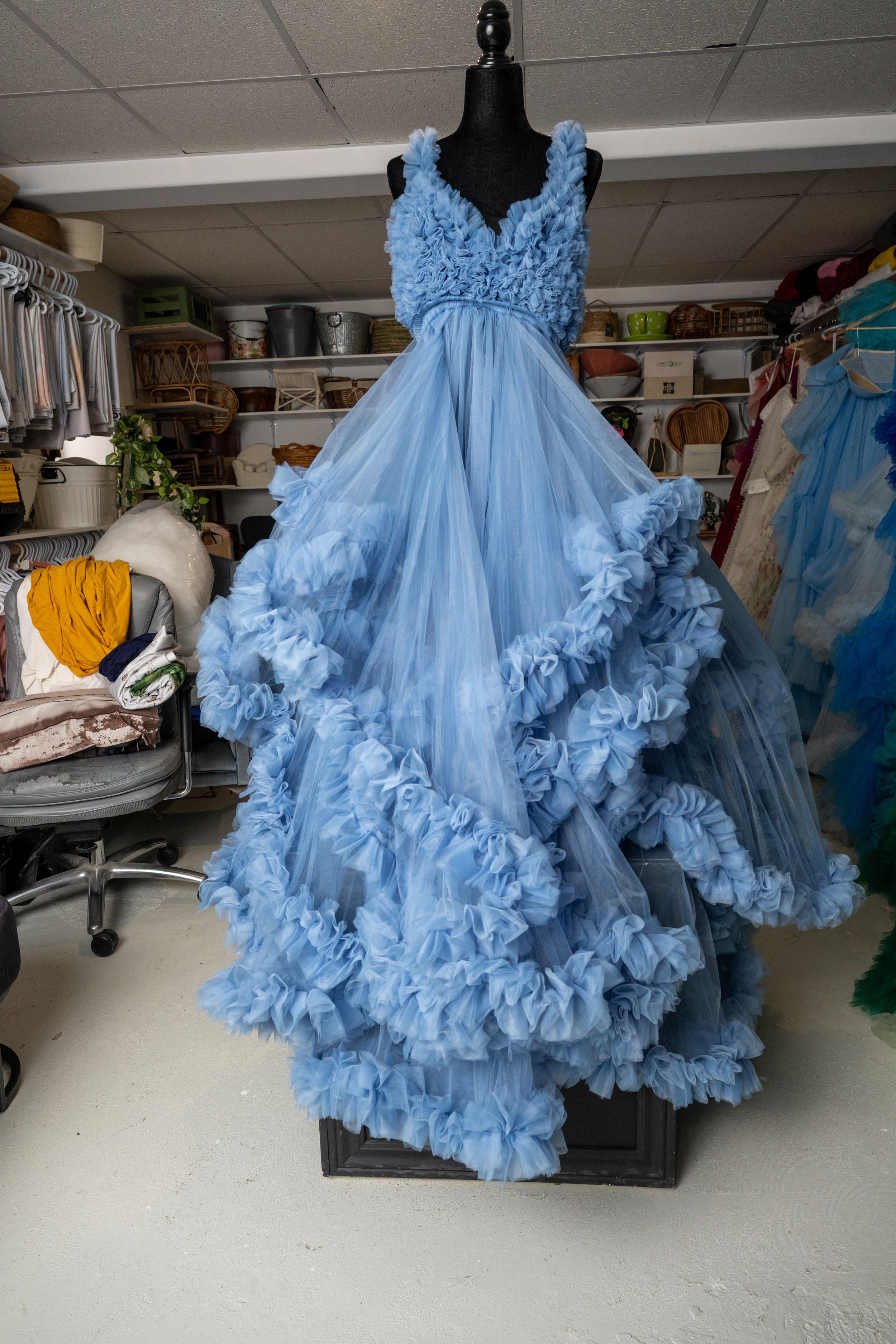 Light blue tulle ball gown with ruffled layers and cloud-like texture displayed on a dress form in a studio setting.