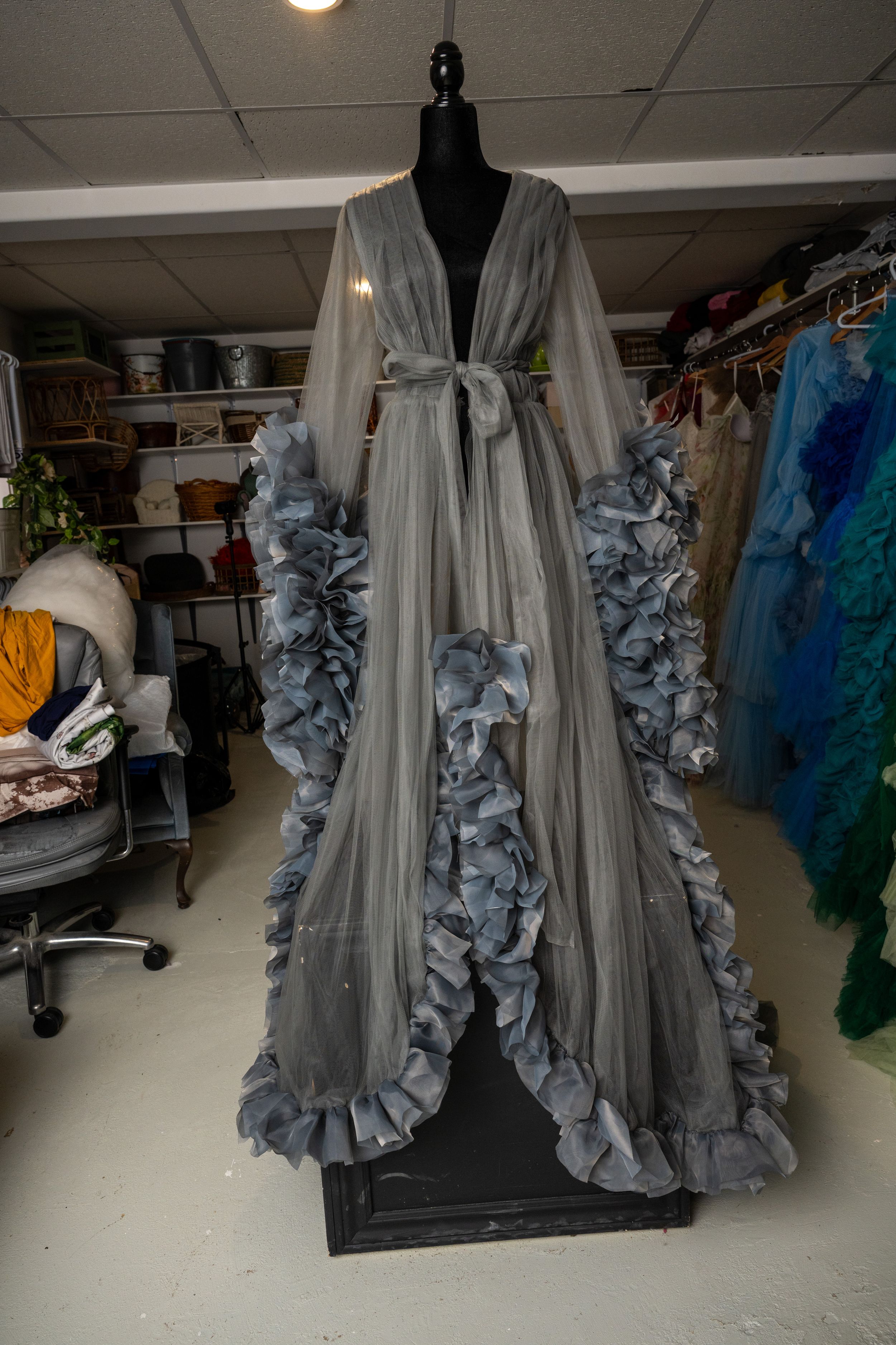 A gray robe with dramatic ruffled details is displayed on a dress form in a studio setting.
