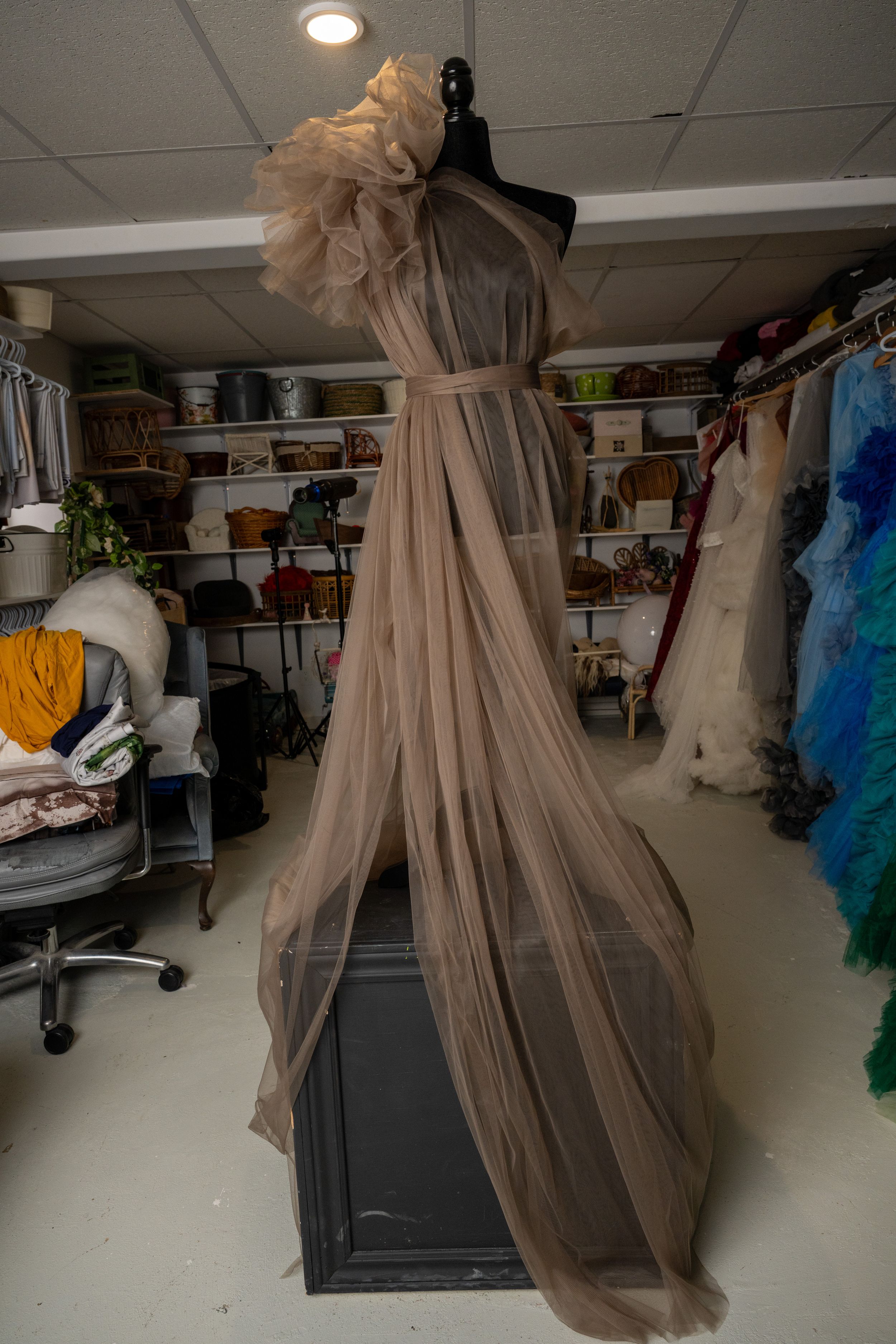 A series of costume racks in a theater wardrobe room showing beige tulle gowns and colorful theatrical garments.