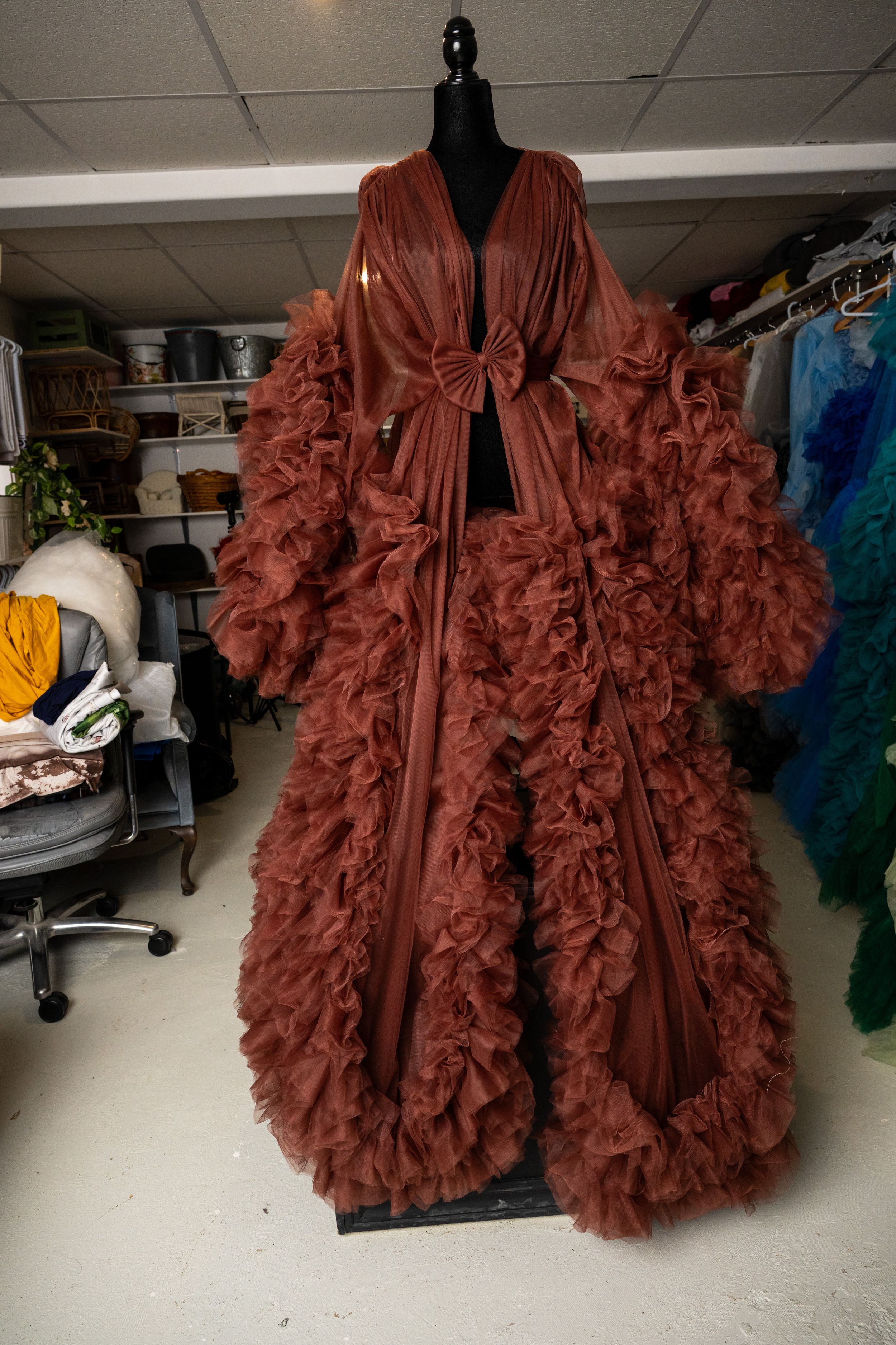 Dramatic burgundy ruffled dressing gown with voluminous sleeves displayed on black mannequin in storage room.
