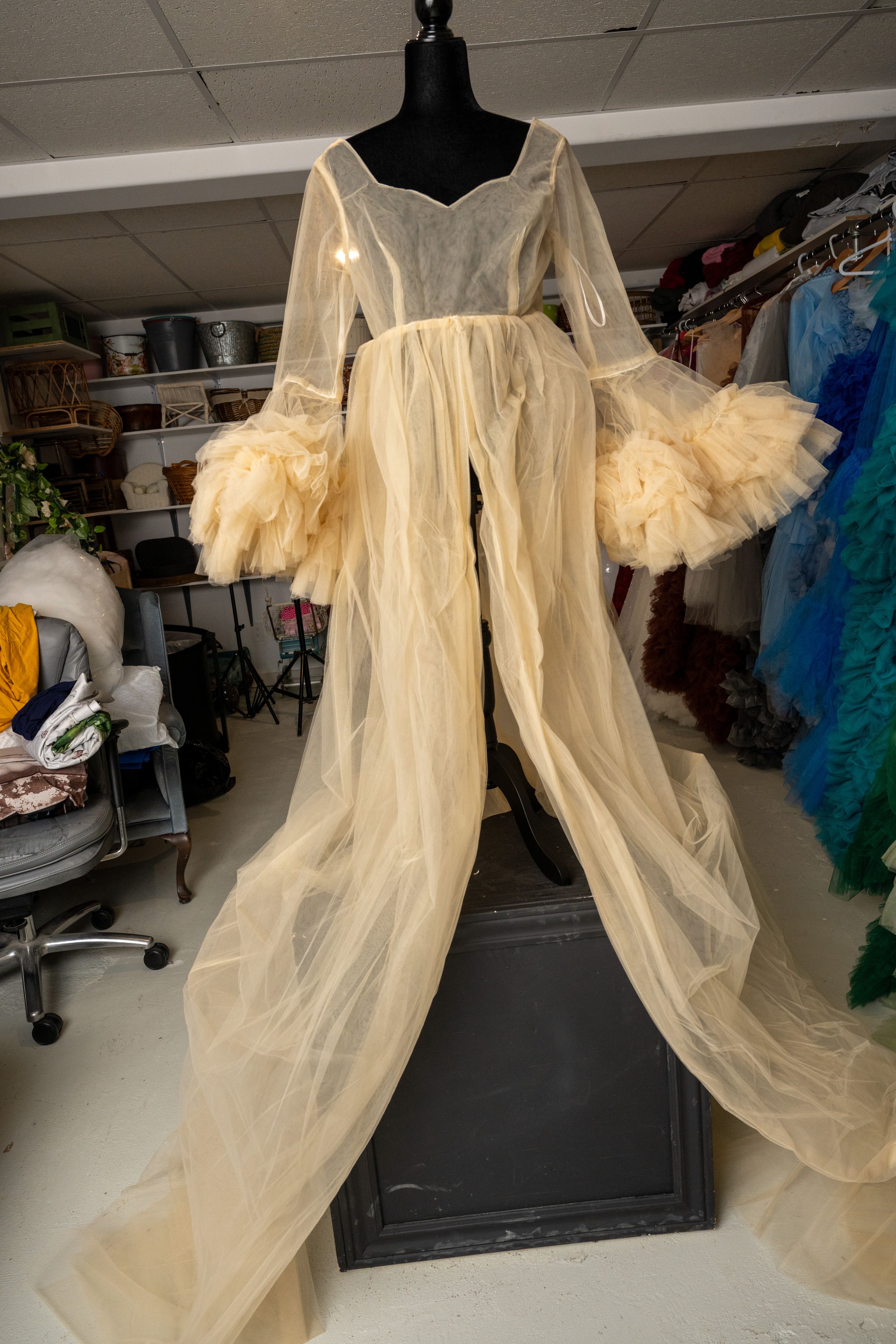 Elegant cream-colored tulle gown with dramatic puff sleeves displayed on a black mannequin in a wardrobe setting.