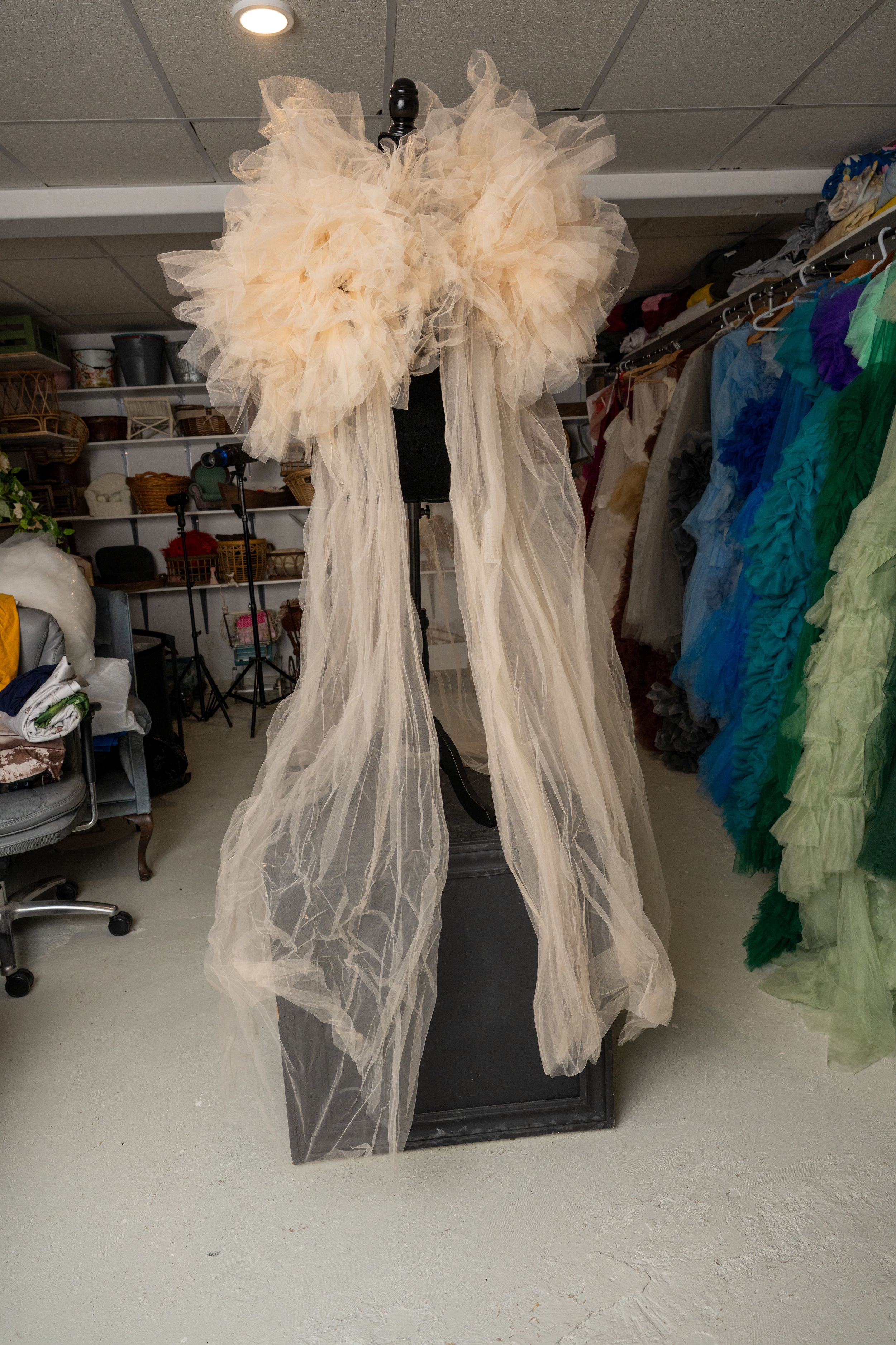 Ethereal white tulle and feather costumes hanging from the ceiling in a storage area with colorful garments visible.