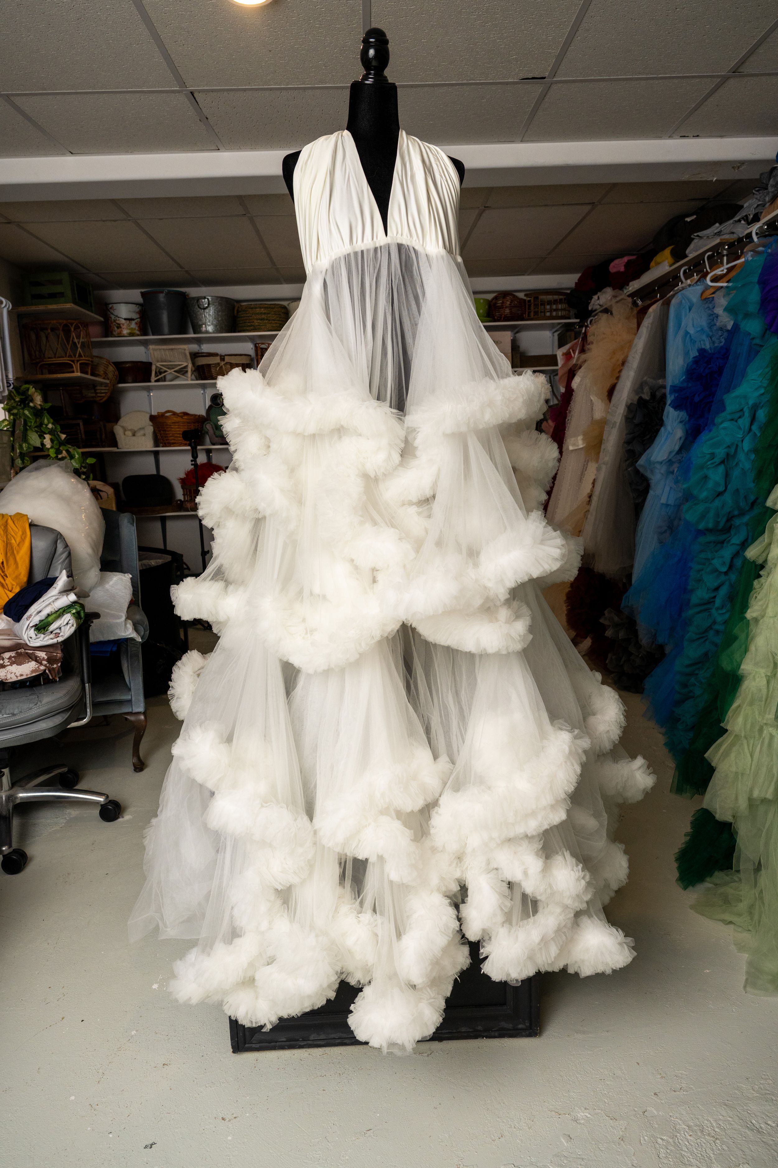 Dramatic white tulle dress with voluminous ruffles displayed on a mannequin in a costume storage room.