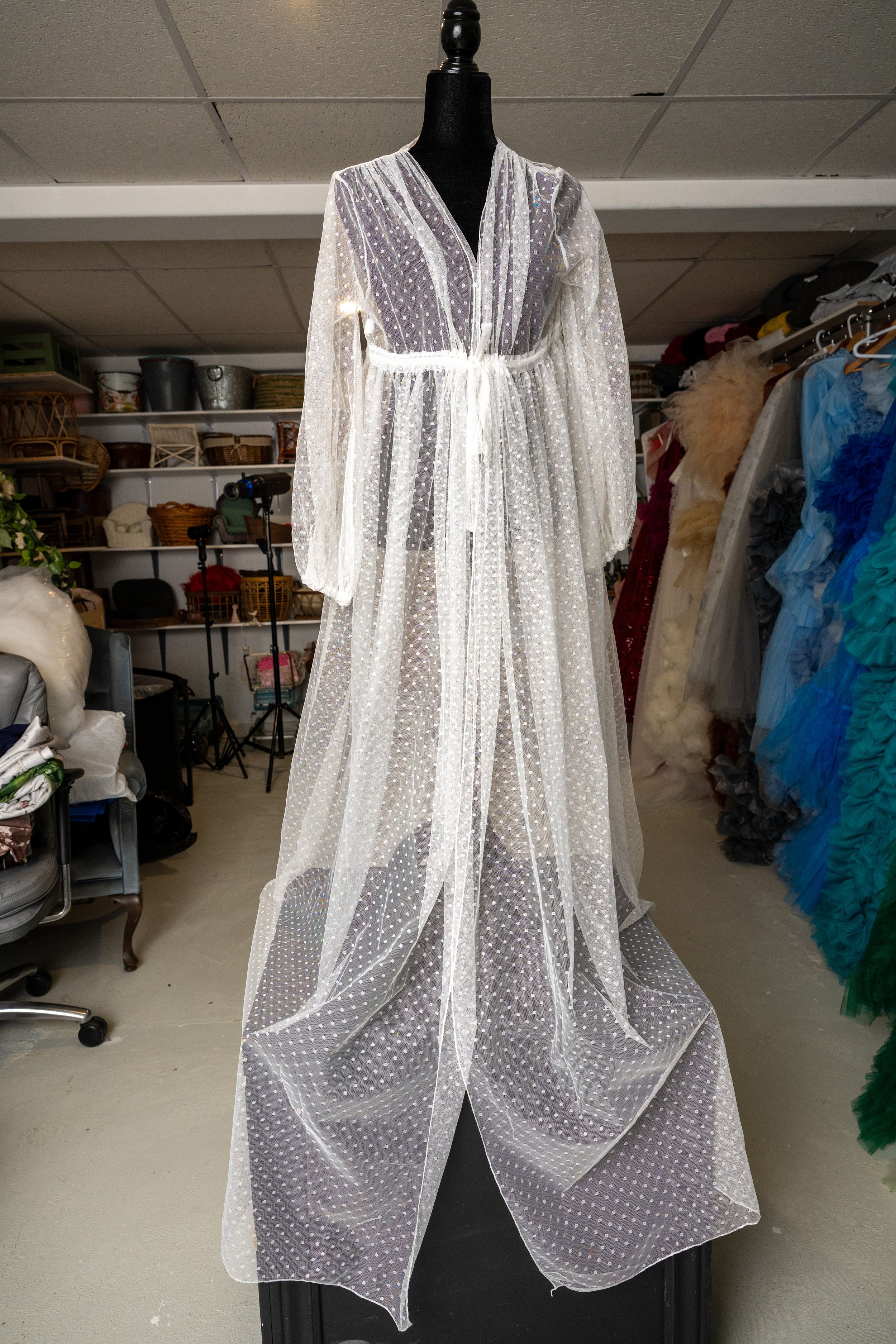 Sheer white polka dot overlay dress shown on a dress form in a wardrobe storage space.