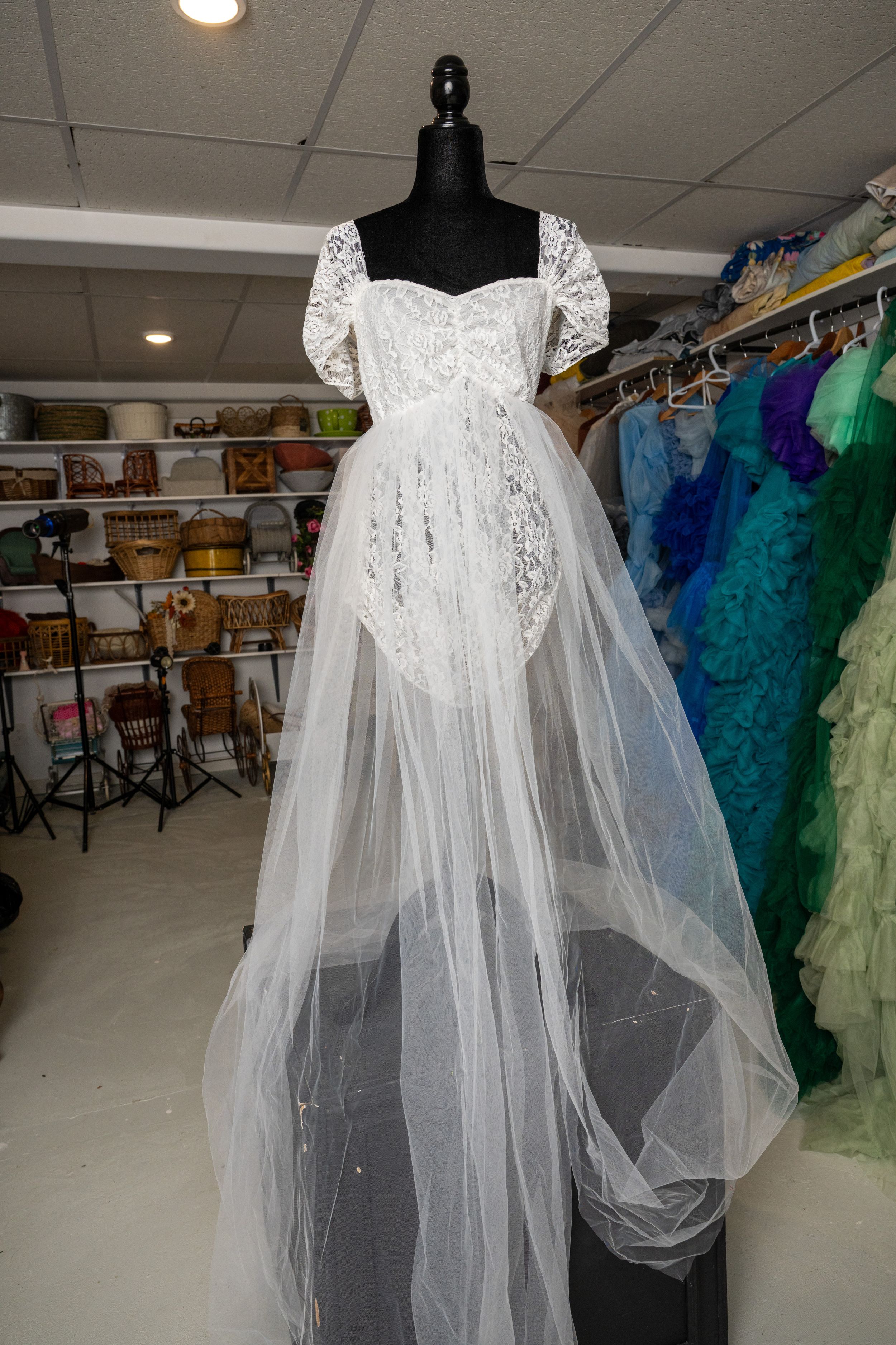 A delicate white lace and mesh nightgown with flowing sleeves shown on a black mannequin in a wardrobe room.