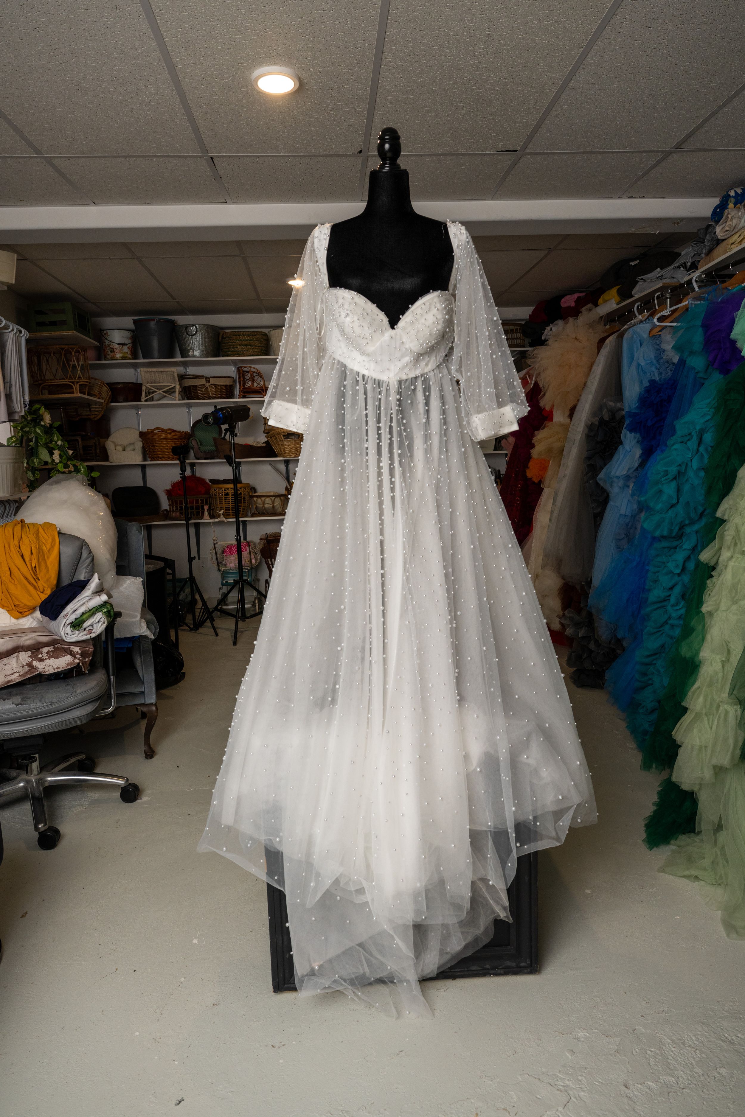A white lace and tulle vintage-style nightgown displayed on a black dress form in a costume storage room.