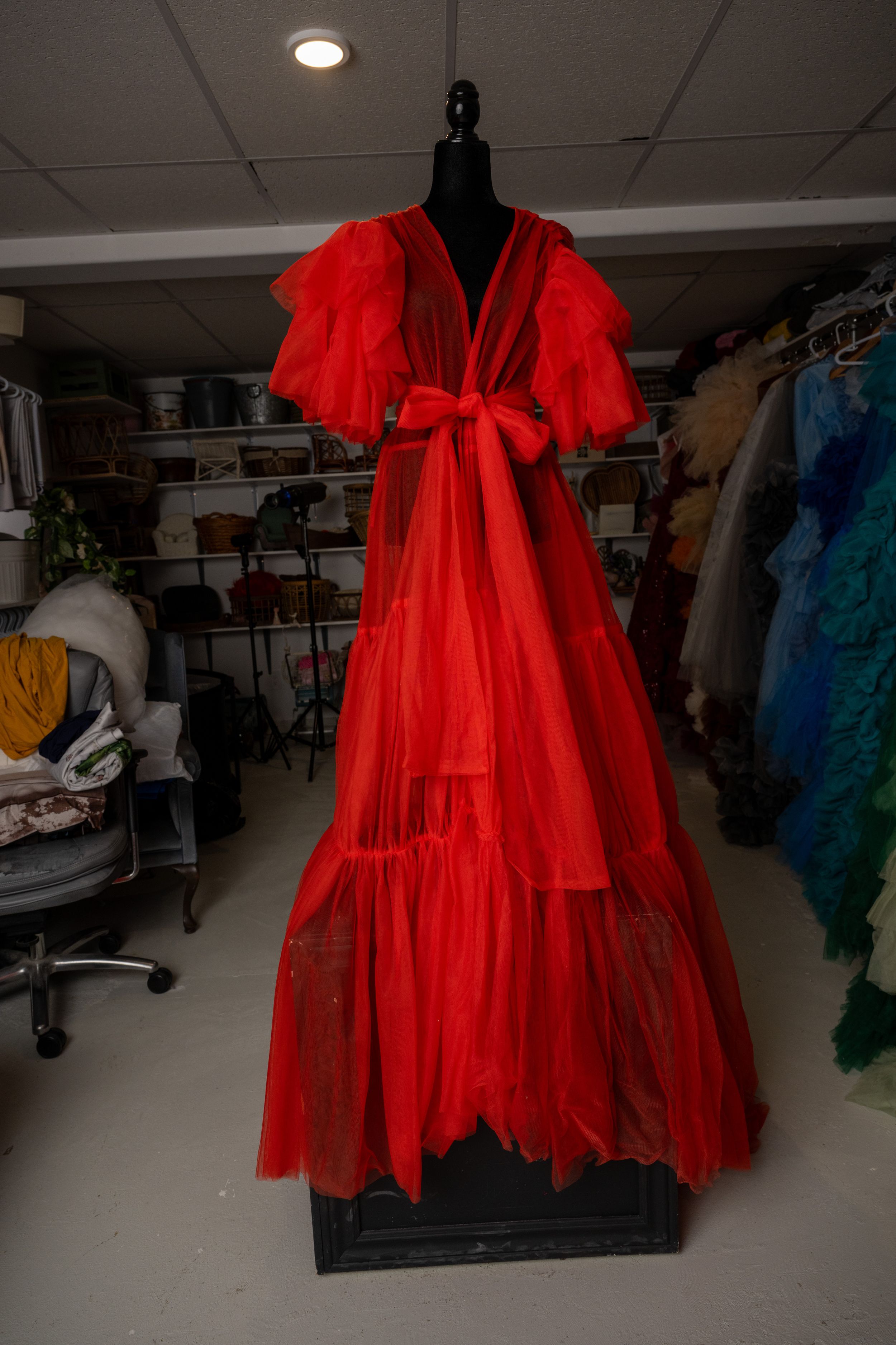 Bright red flowing dress with dramatic ruffled sleeves displayed on a mannequin in a costume room.