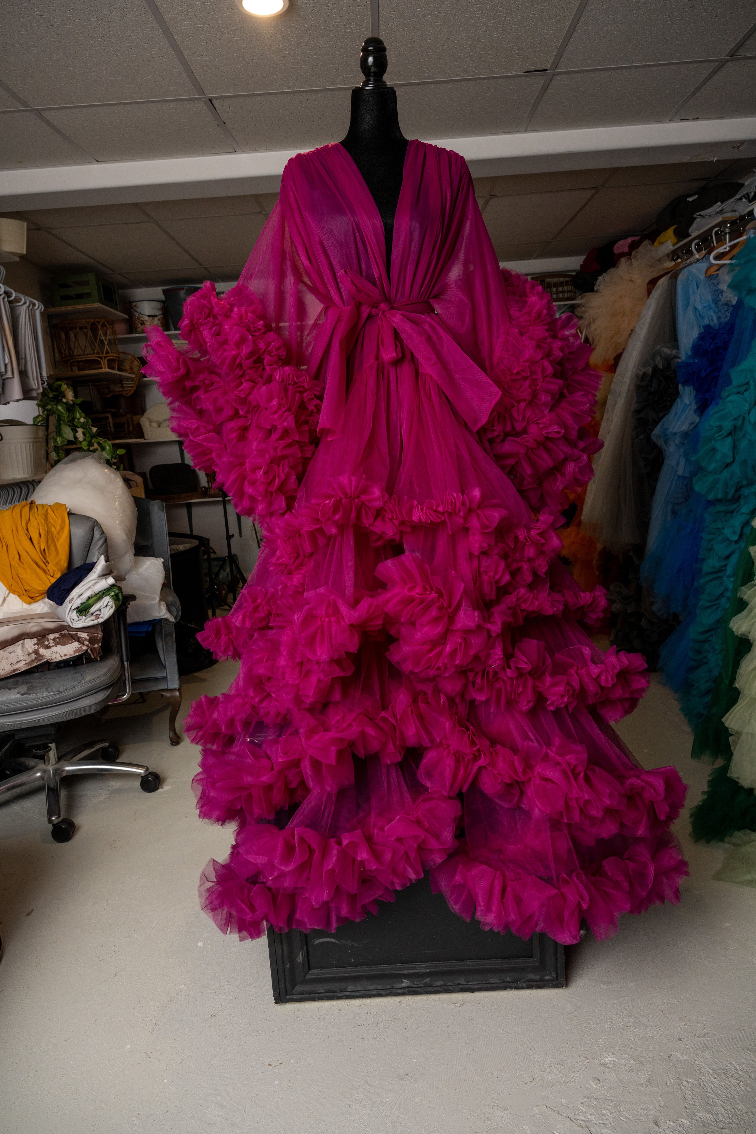 Luxurious hot pink sheer robe with dramatic ruffled tulle details displayed on a black mannequin in a dressing room.