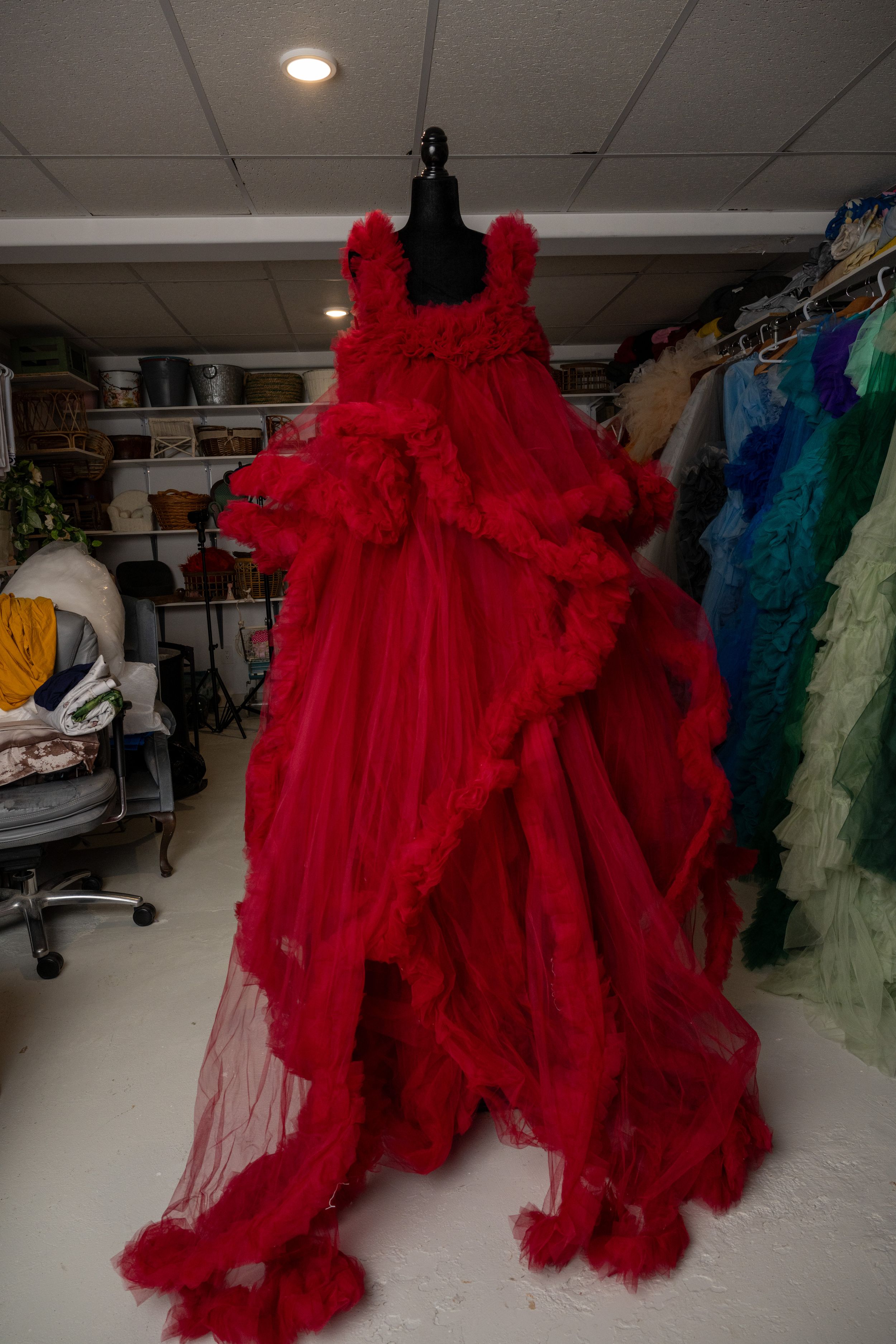 A vibrant red tulle gown with dramatic ruffles and layers is displayed in a bridal shop among other formal dresses.