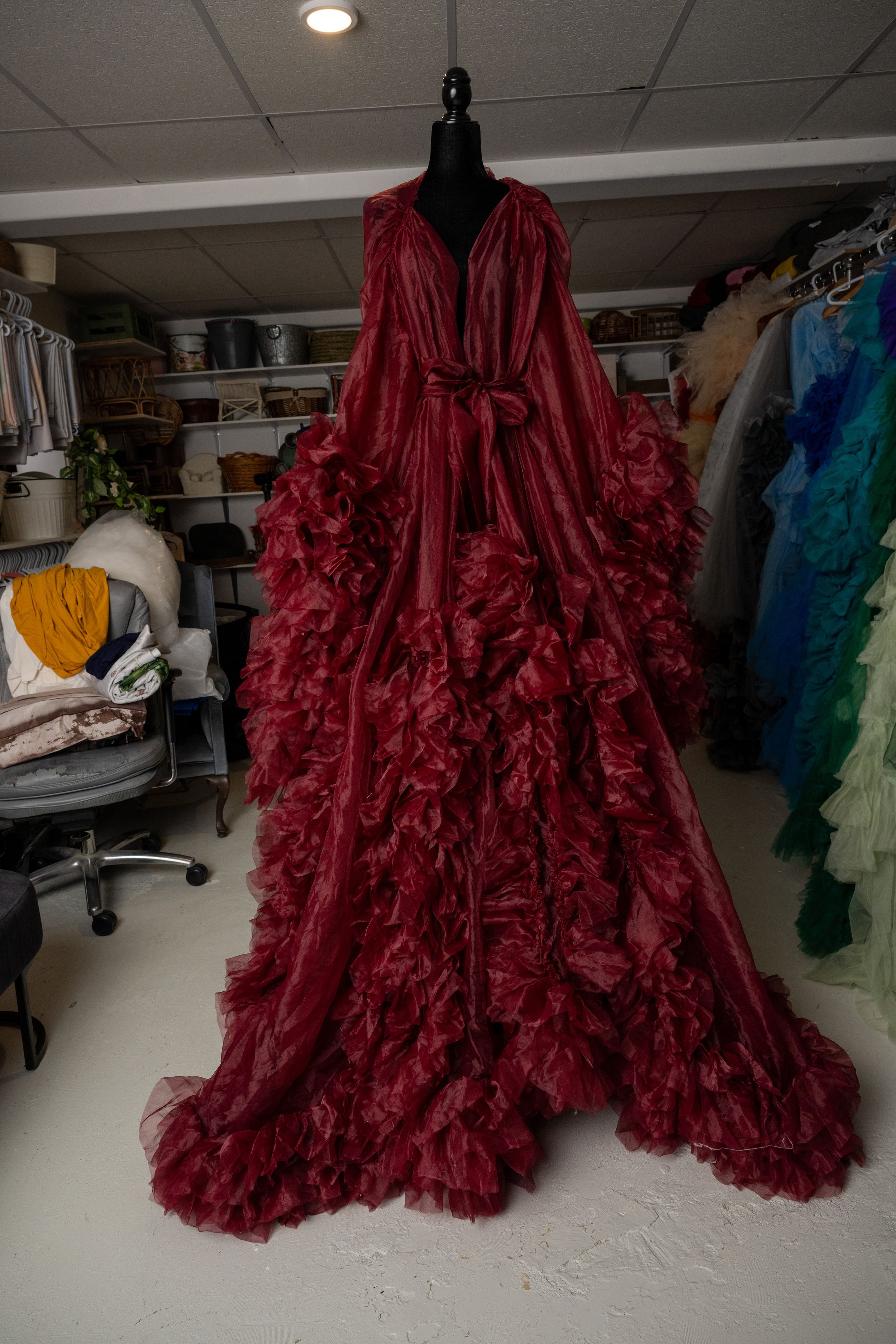 A luxurious deep red ruffled robe with dramatic flowing sleeves displayed on a mannequin in a wardrobe room.
