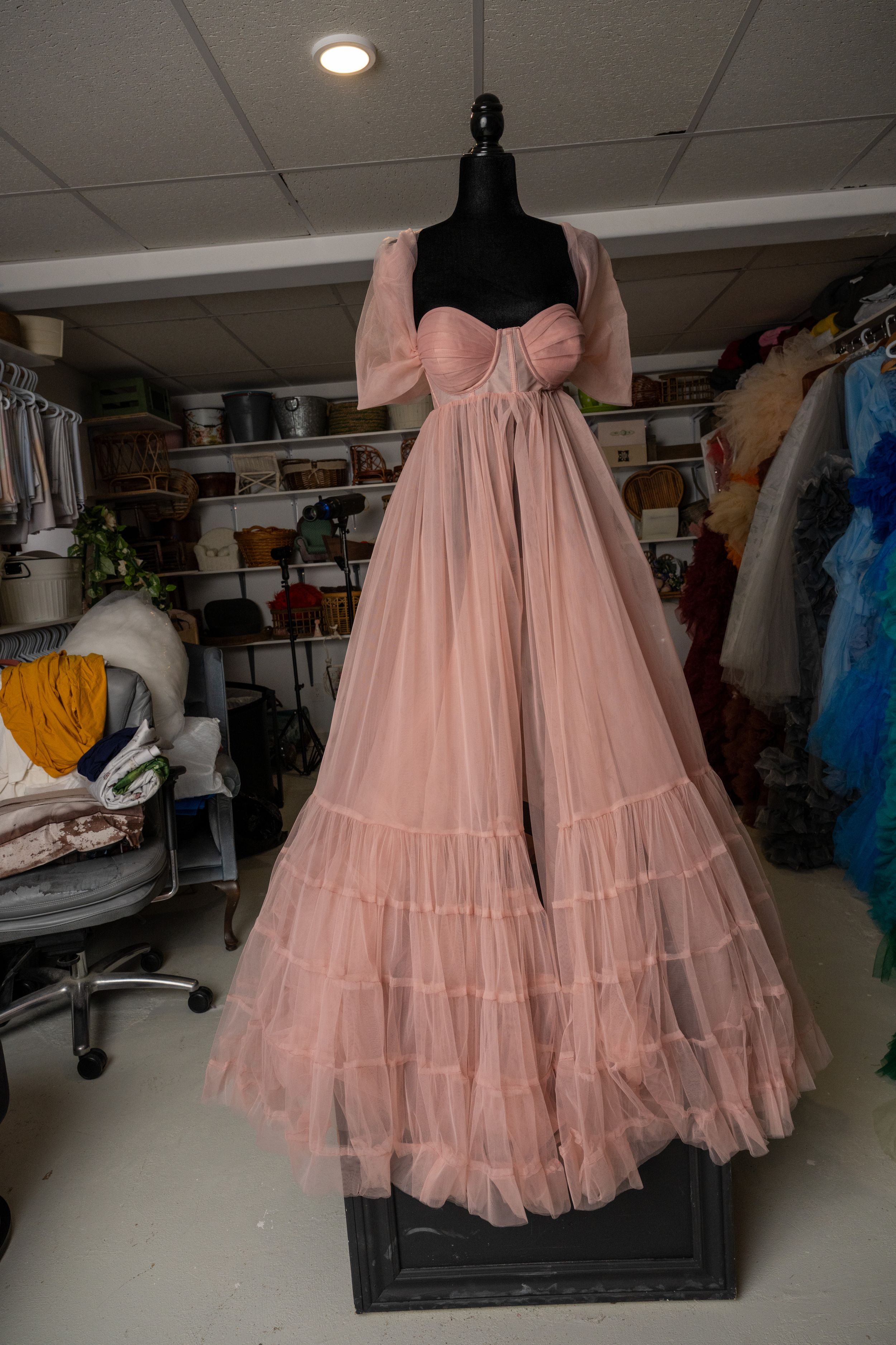 Pink tulle vintage-style petticoat dress displayed in a storage room with other formal gowns.