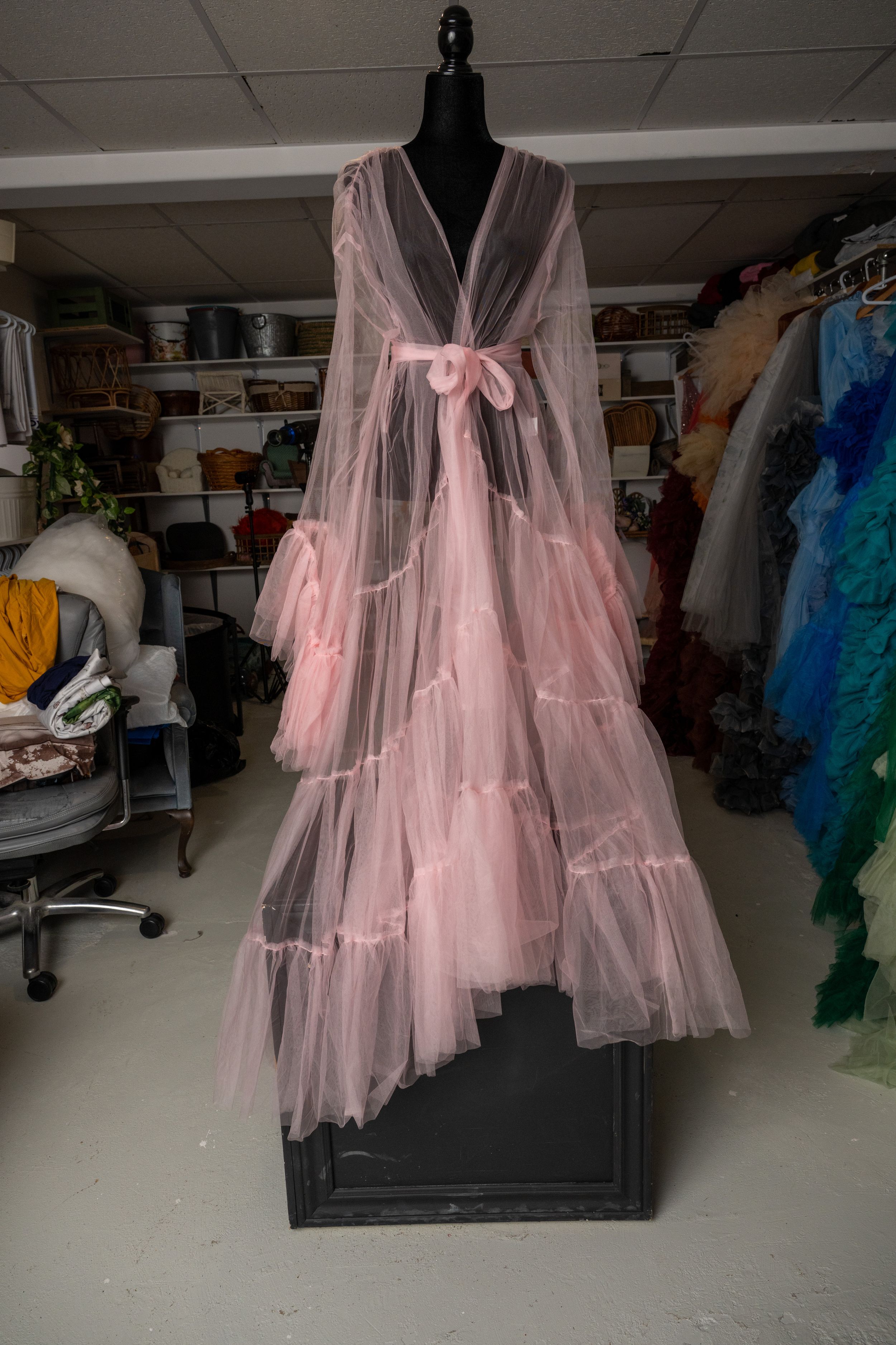 Pink tulle dresses on display in a dimly lit storage room or wardrobe area.