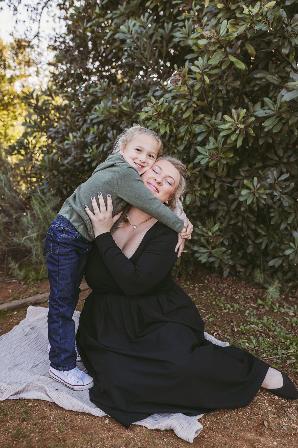 Playful interaction between child and adult on a blanket outdoors with greenery in the background in Redlands,CA.