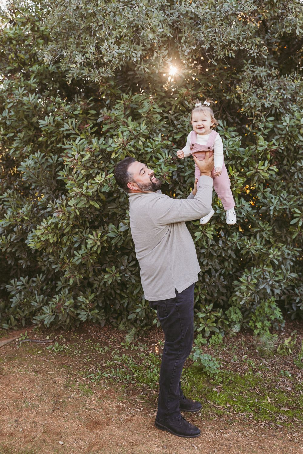 A heartwarming sequence of photos shows a parent lifting and playing with a small baby against a green hedge background.