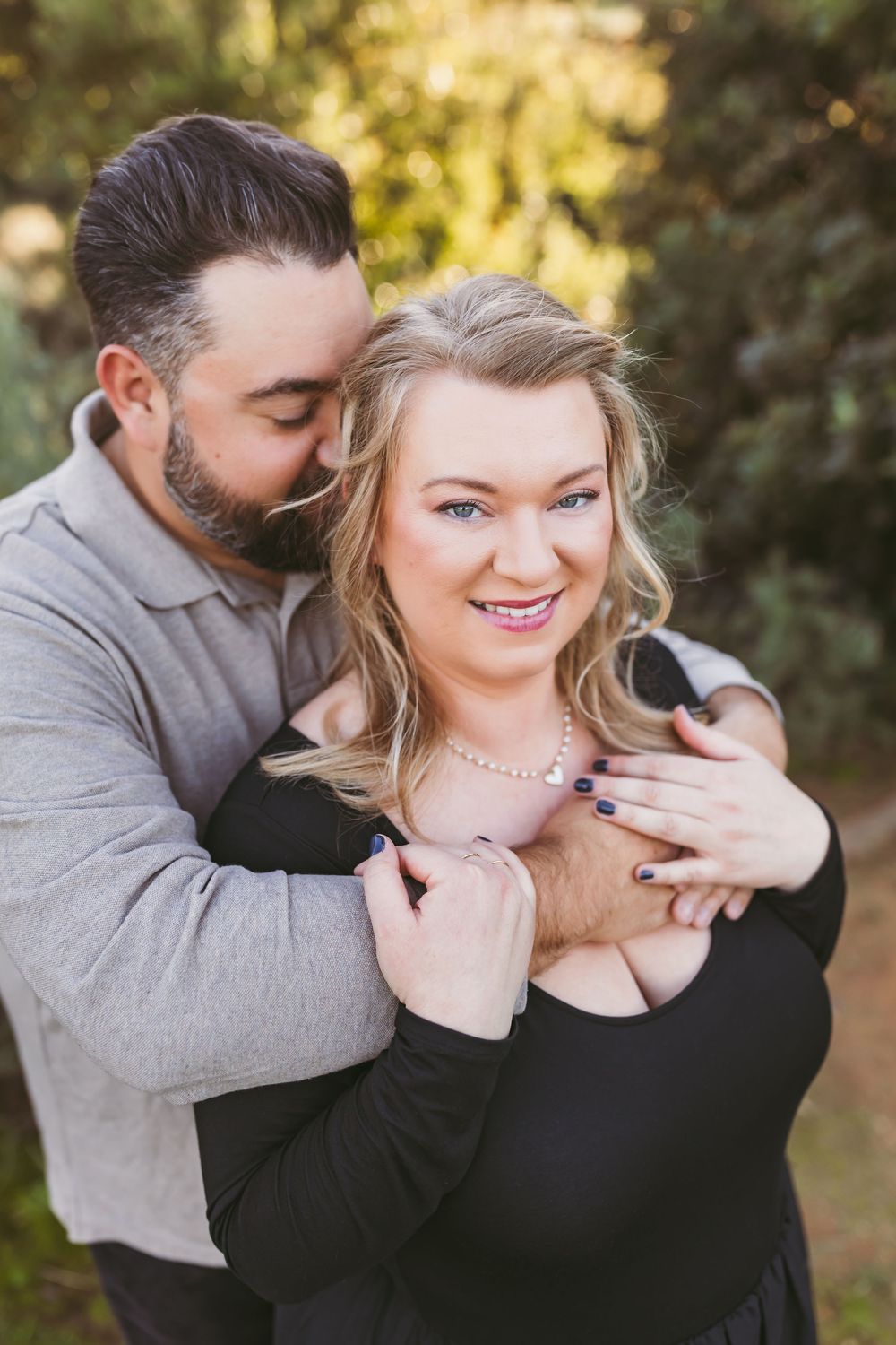 A couple embraces outdoors in romantic portrait series with soft natural lighting and coordinated black and gray outfits.