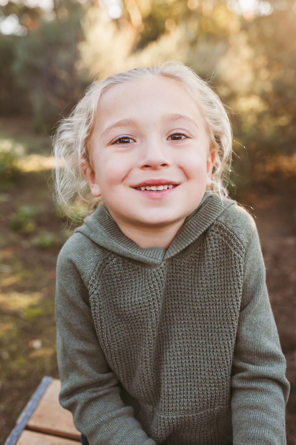 A series of four close-up shots showing a child in a gray knit sweater expressing joyful emotions outdoors.