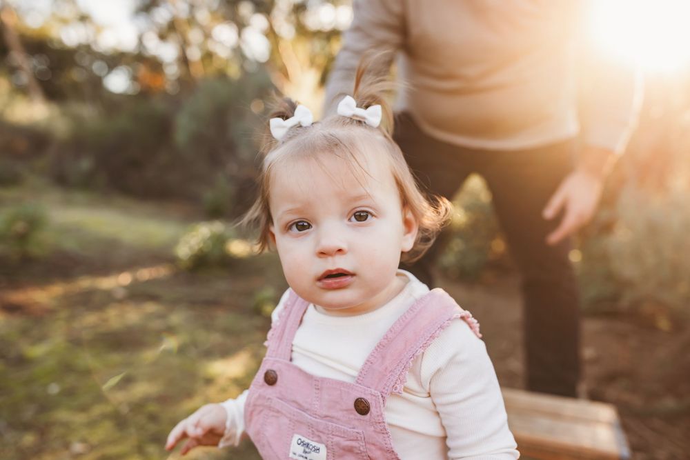 A series of warm sunset photos showing a baby in pink overalls playing outdoors during golden hour.