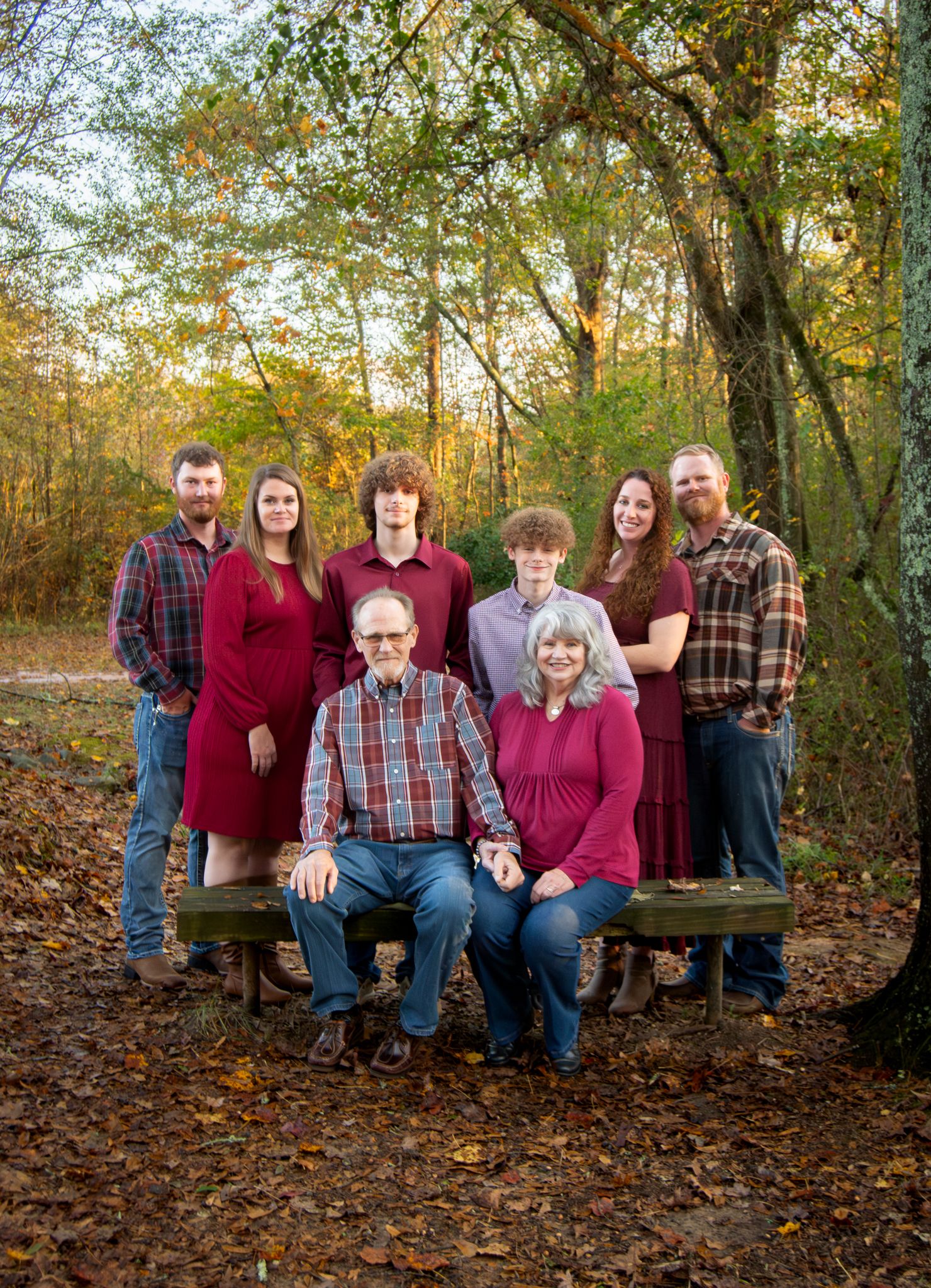 A multi-generational family portrait in casual attire against an autumn woods backdrop.