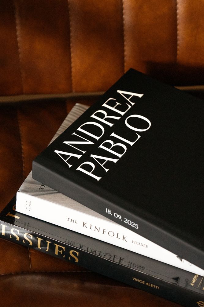 Several black hardcover books with white text are stacked at an angle on a dark wooden surface.