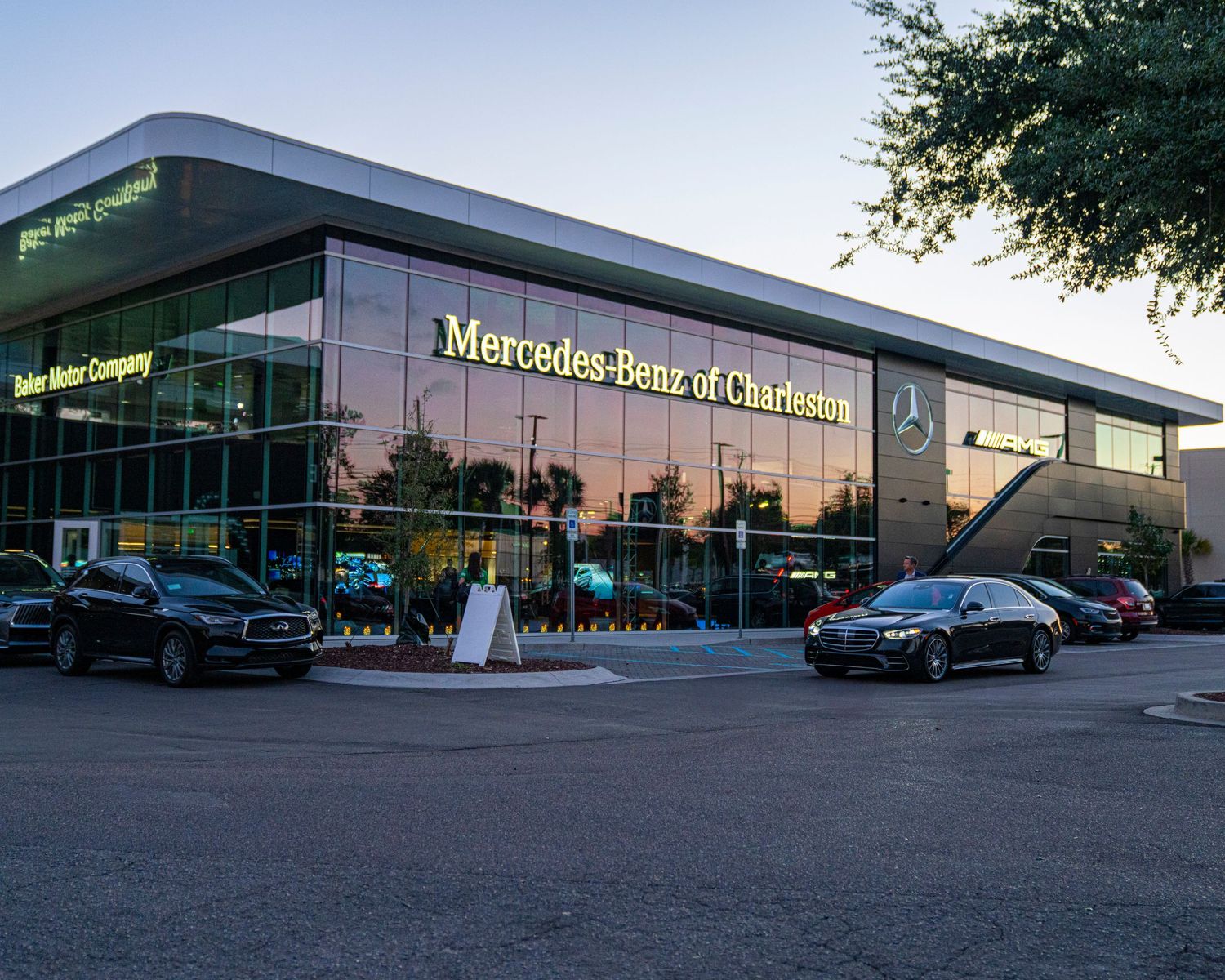 Modern Mercedes-Benz dealership building with glass facade reflecting sunset light in an urban setting.