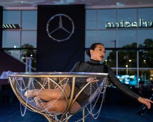 A person performs an acrobatic dance move in front of a Mercedes-Benz dealership at night.