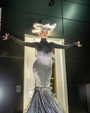 Performer in a sparkly silver dress poses dramatically against a dark wall during an artistic photoshoot.