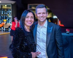 A couple poses together at an evening event, with the woman wearing a sparkly black dress.