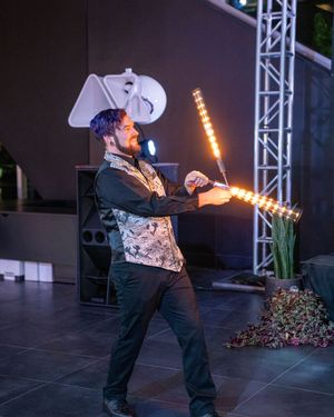 Performer in black attire and white hat does a dramatic pose with illuminated props on stage.