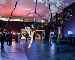 Aerial acrobatic performance under pink and blue lighting with suspended equipment.