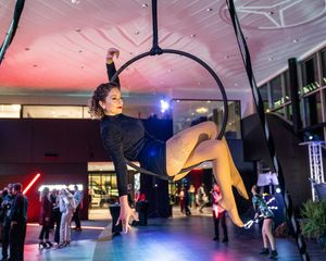 A group of dancers perform synchronized aerial moves using suspended ropes in a dimly lit studio space.