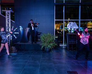 Performers in dark lighting create a dynamic scene with a violinist and dancers on stage.