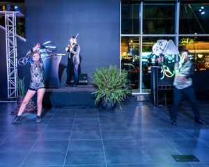Dancers perform an energetic routine against a blue wall with stage lighting and truss structures.