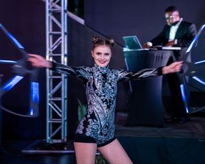 Dancers performing choreographed moves on a dark stage with dramatic blue lighting and technical equipment.