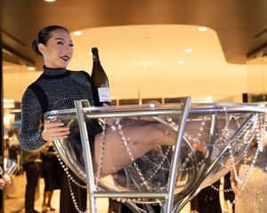 A performer pours champagne into a large martini glass display at an elegant indoor venue.