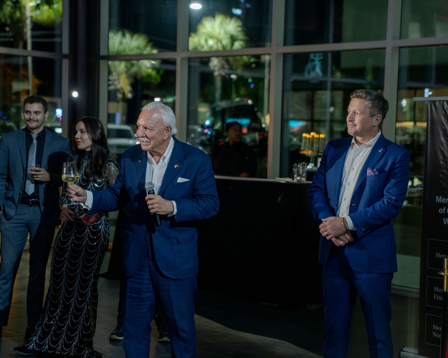 A group of people in blue suits stand together during an evening event on a patio.