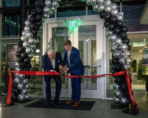 A ribbon cutting ceremony with silver balloon arch decorations at a business entrance.