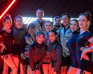 A group of performers pose together under dramatic red neon lighting at a nighttime event.