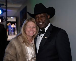 Two people pose together at a formal event, with one wearing a black cowboy hat and tuxedo and the other in a fur coat.