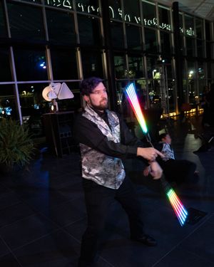 Entertainer performs with glowing LED light sticks against a glass building backdrop at night.