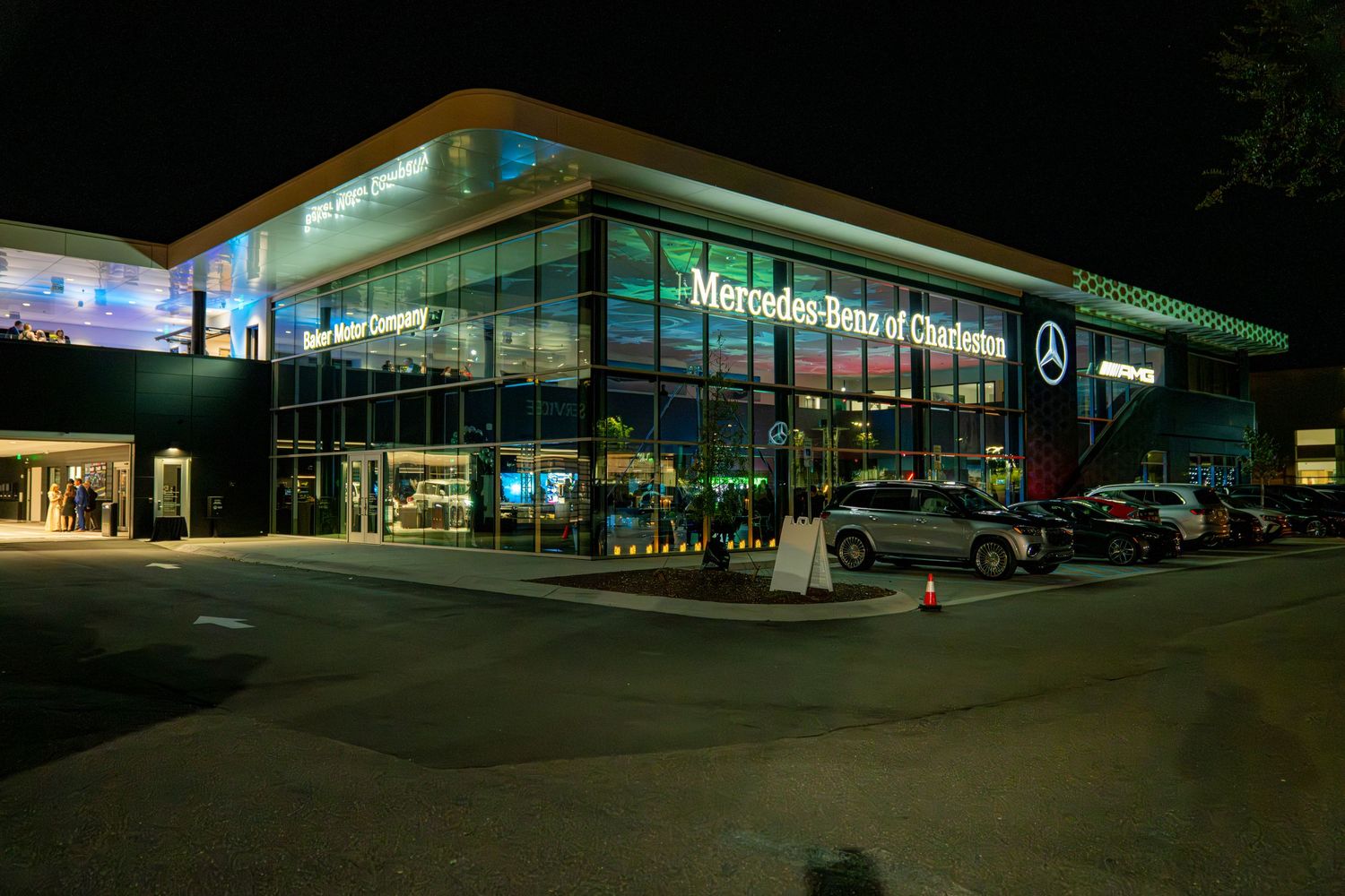 Mercedes-Benz dealership illuminated at night with modern architecture and multiple cars on display.